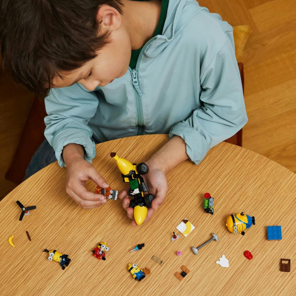 Çocuk ahşap masada Minion figürleri ve parçalarıyla Lego muz araba yapıyor.