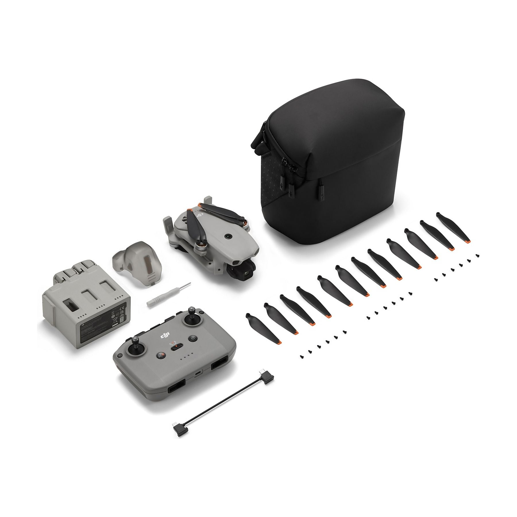 Drone grigio, controller, batteria, borsa, eliche e viti su sfondo bianco.