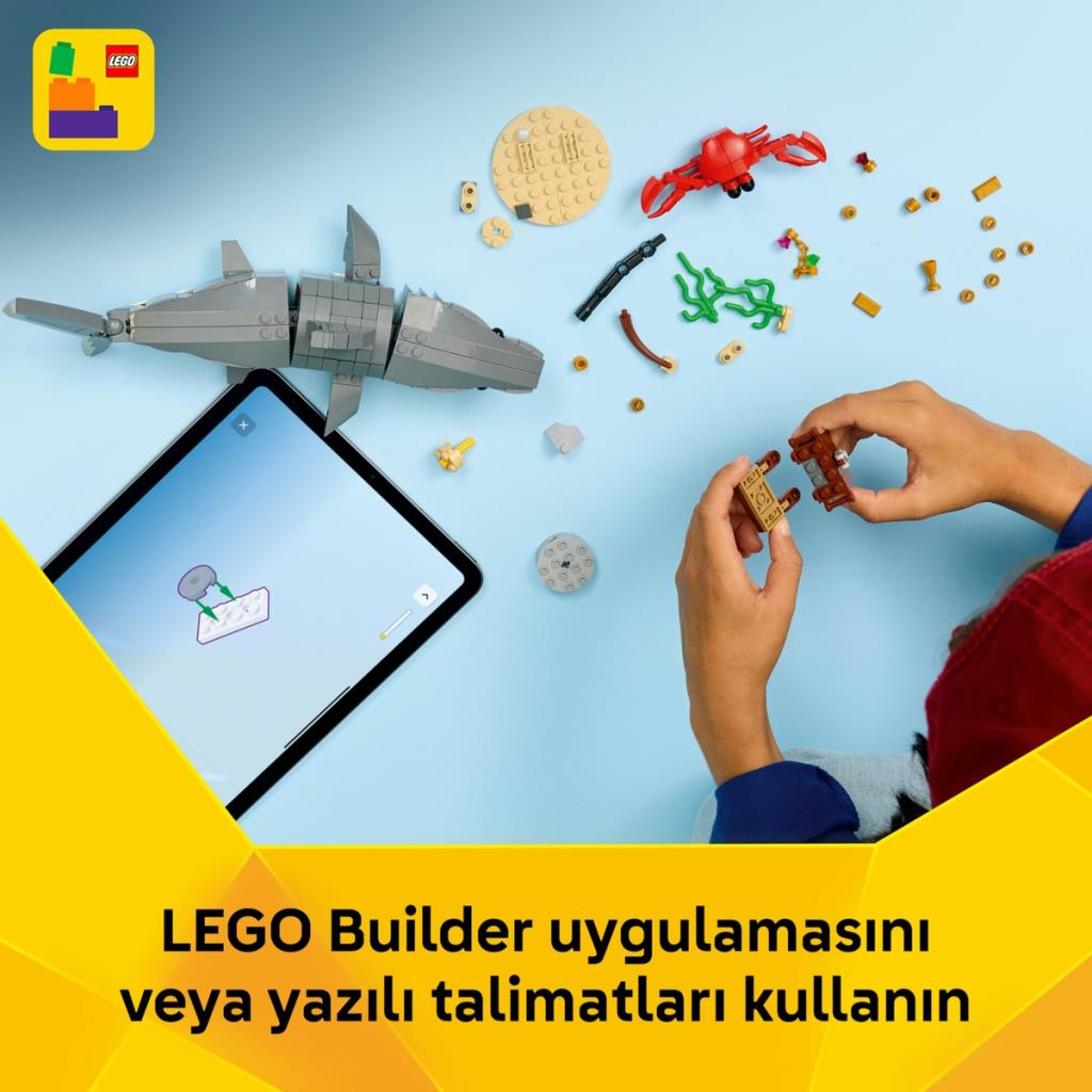 Un tiburón gris de Lego descansa sobre una superficie azul con ladrillos Lego dispersos y una tableta.
