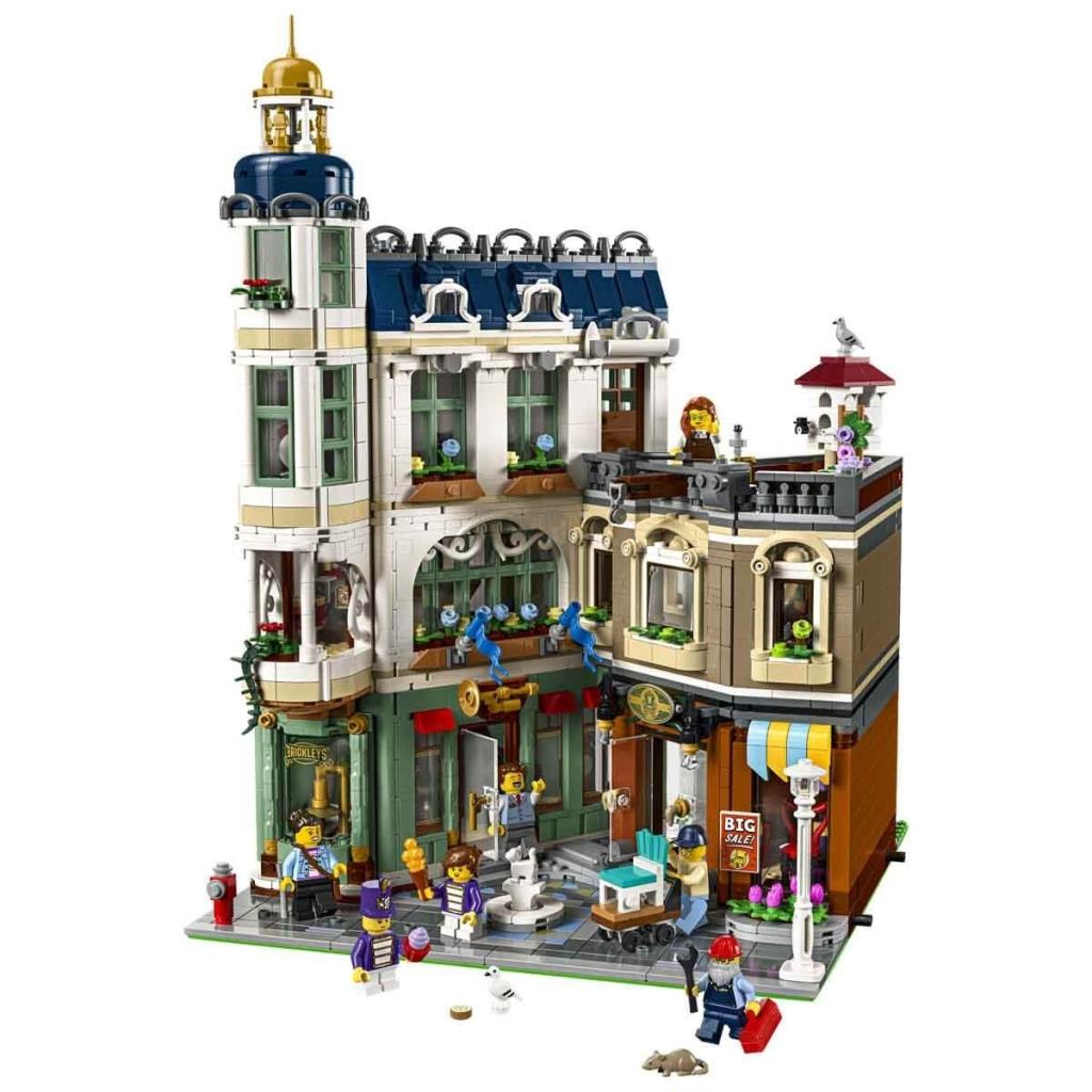 Beyaz arka plan üzerinde dükkanlar ve figürler bulunan çok katlı Lego bina.