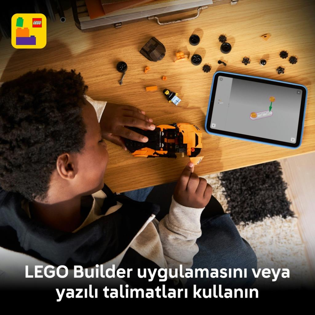 Dziecko buduje pomarańczowy samochód Lego z instrukcją na tablecie.