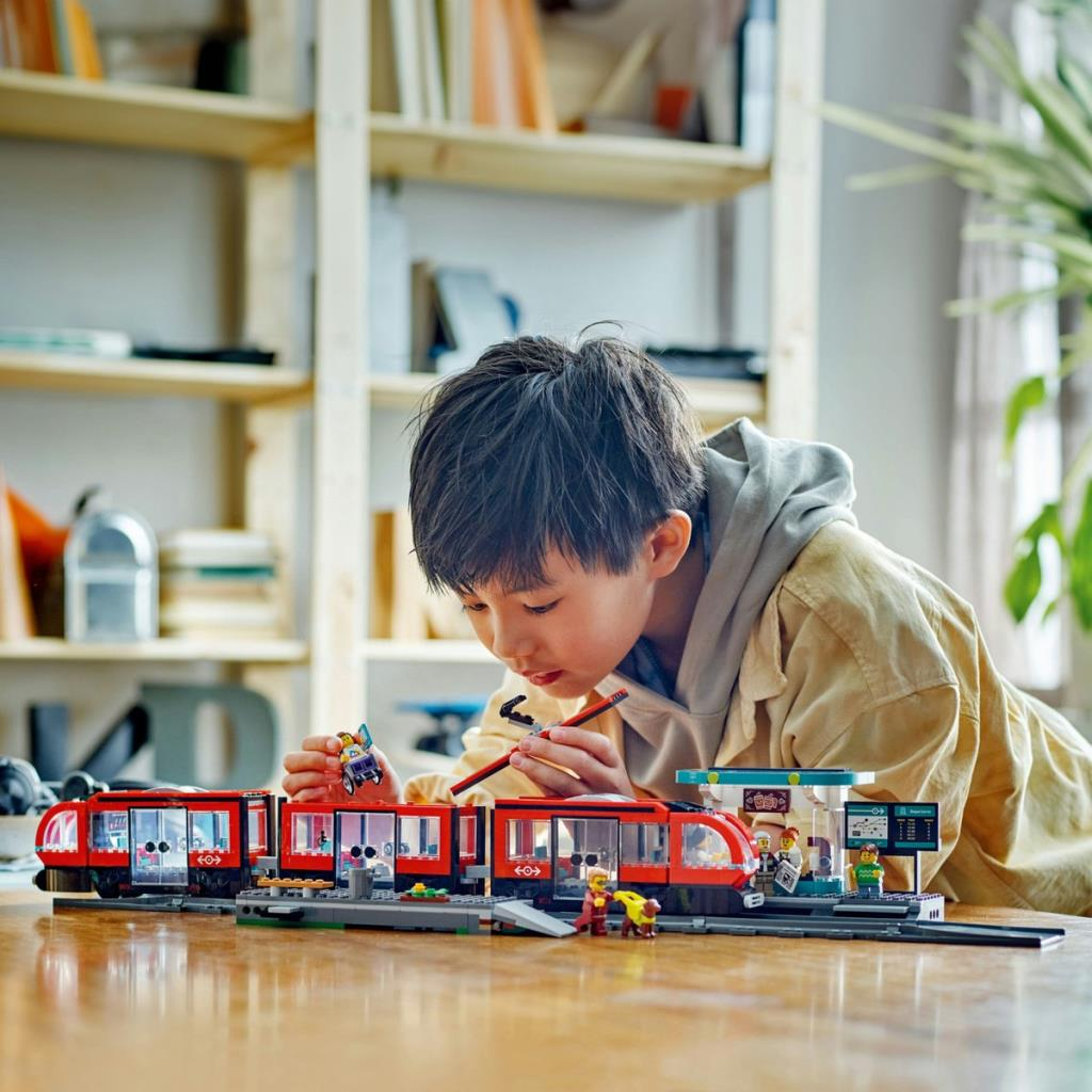 Bir çocuk ahşap bir masada kırmızı bir Lego treni ve istasyon inşa ediyor.