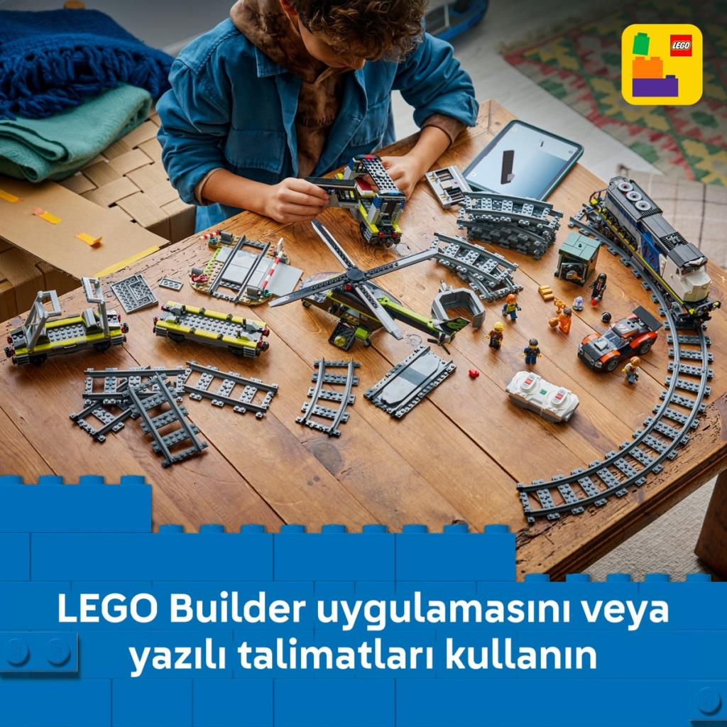 Bir çocuk ahşap masada raylarla Lego trenler ve helikopter inşa ediyor.