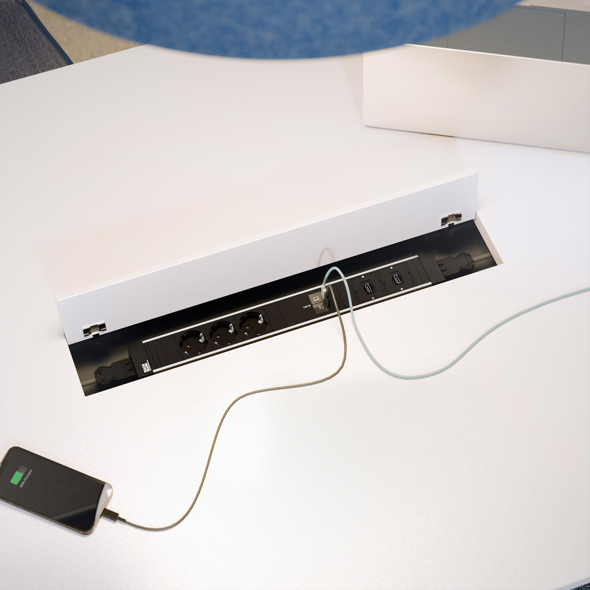 Ein Smartphone wird an eine integrierte Tischsteckdose mit USB-Anschlüssen geladen.
