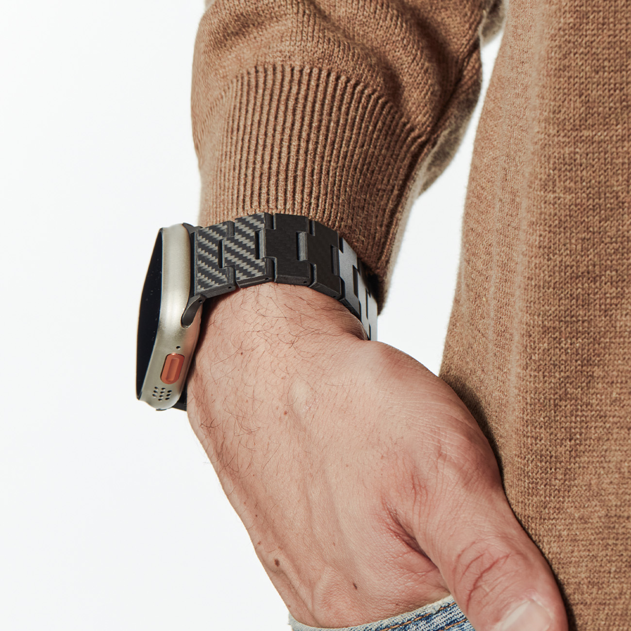 Una persona lleva un smartwatch plateado con correa de fibra de carbono negra y un jersey marrón.