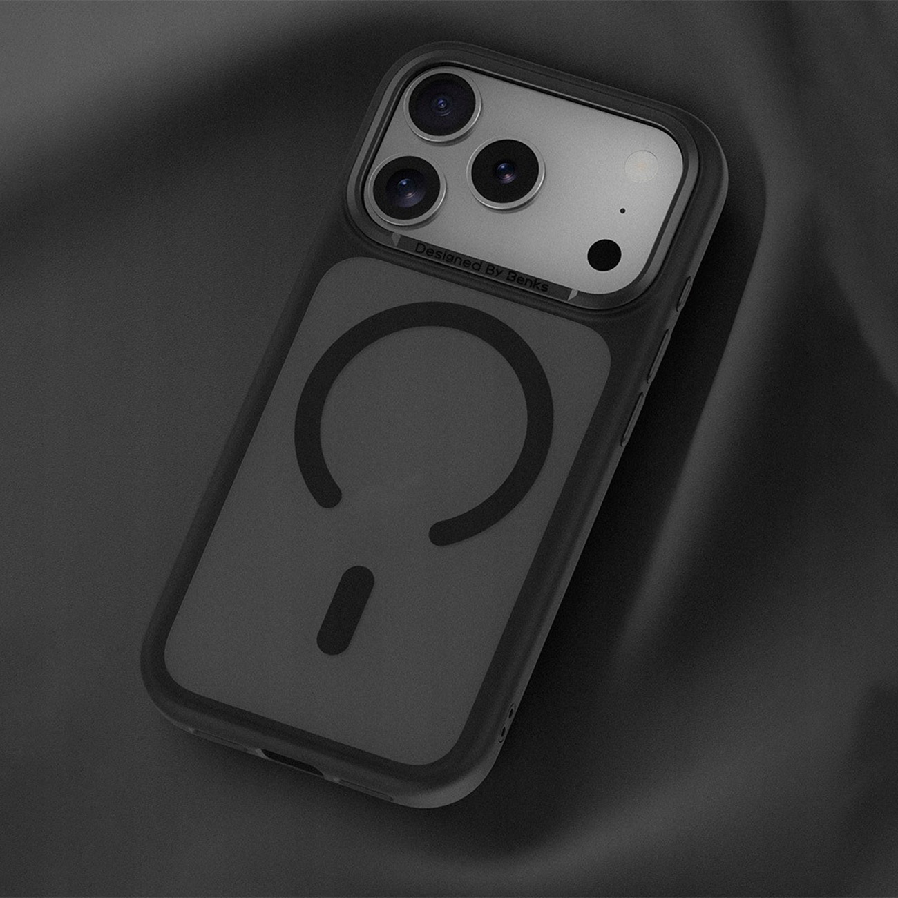 Teléfono negro con tres cámaras y anillo magnético sobre fondo oscuro.