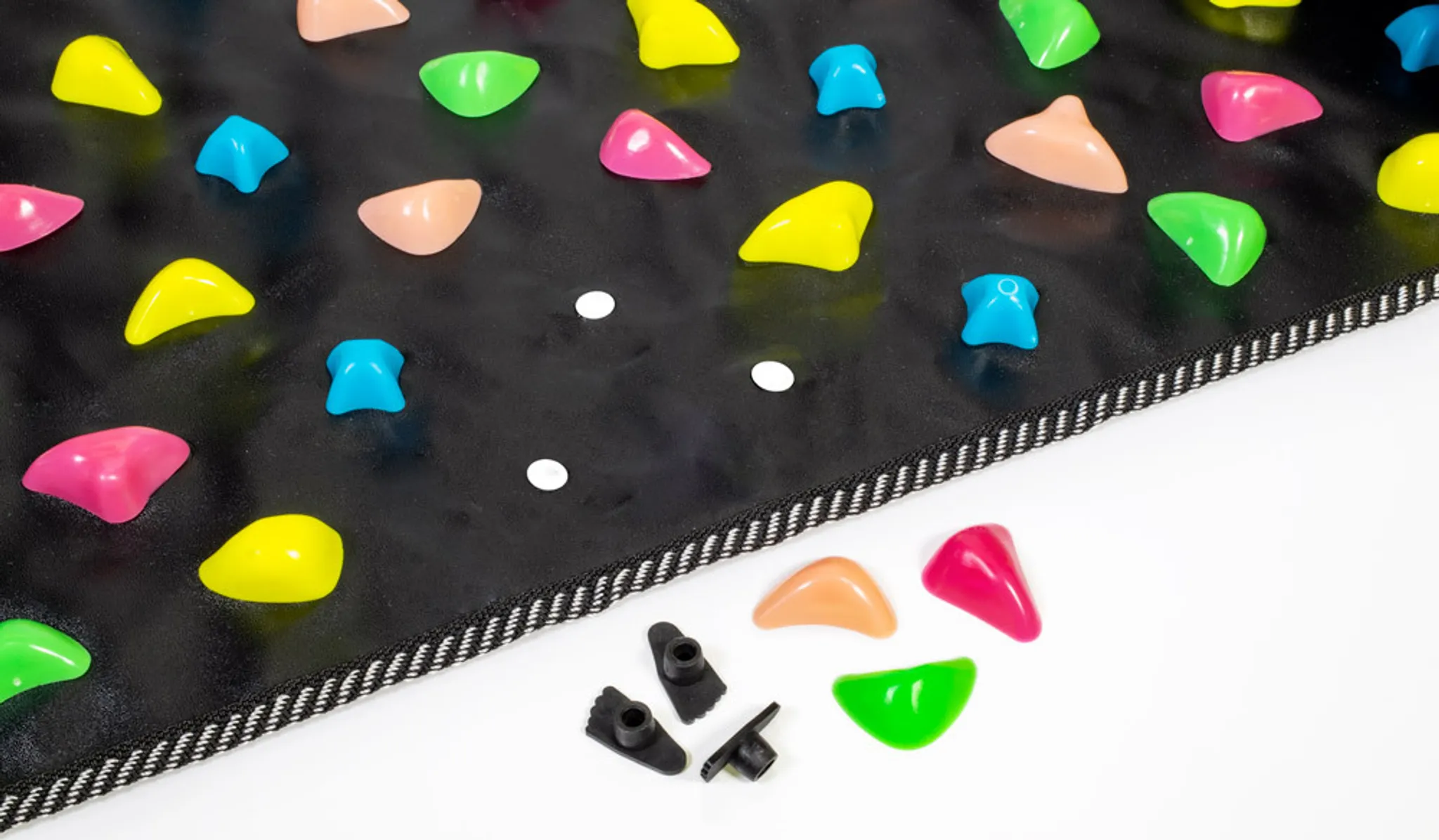 Bunte Klettergriffe auf schwarzem Untergrund mit weißen Punkten und schwarzen Halterungen.