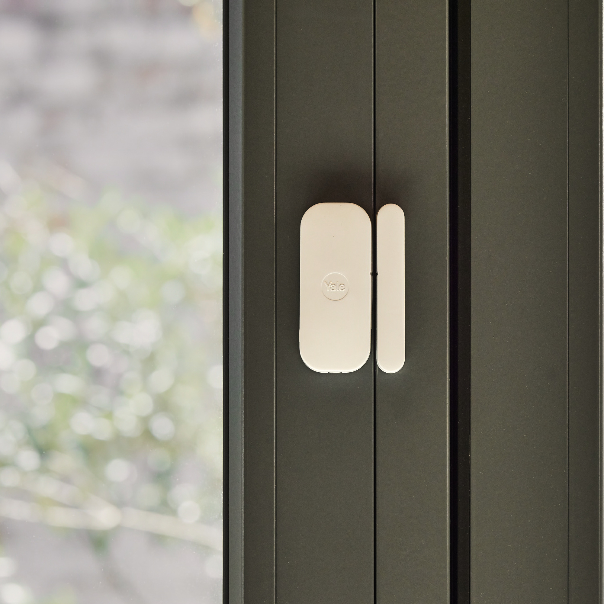 Un sensore bianco Yale per porta/finestra è fissato a un telaio scuro.
