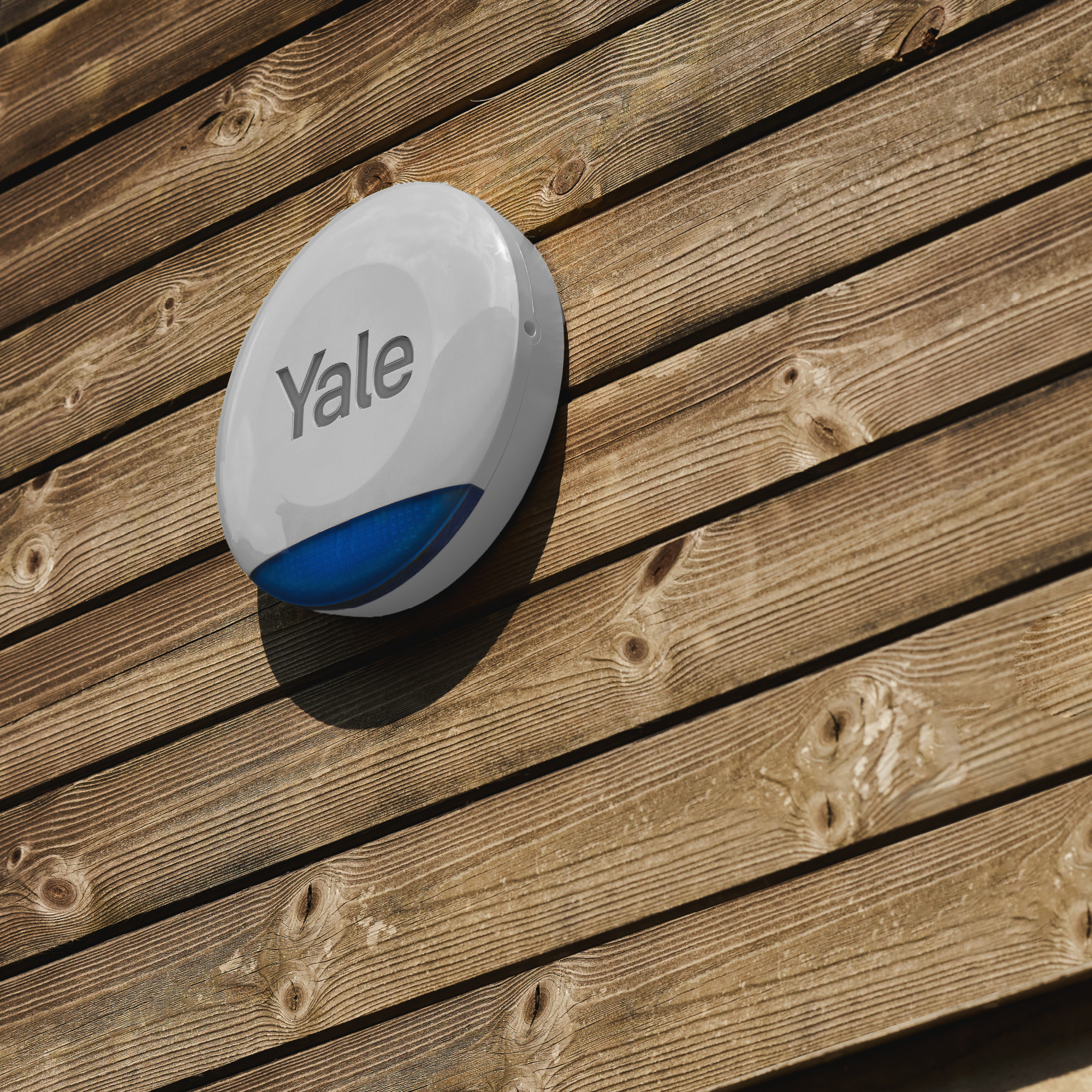 Un rilevatore di movimento bianco Yale con accento blu su assi di legno.