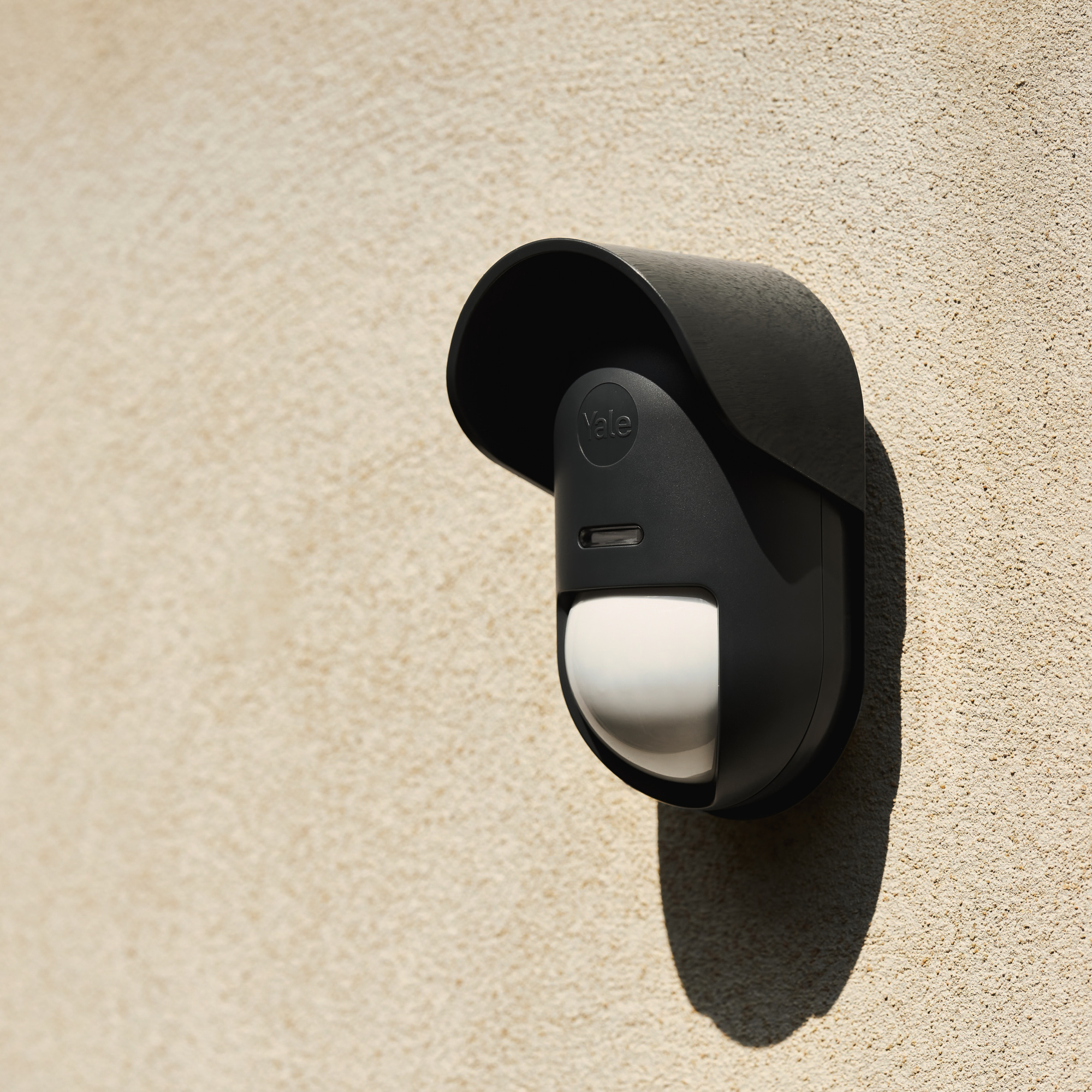 Ein schwarzer Bewegungsmelder mit Yale-Logo an einer hellen Wand.