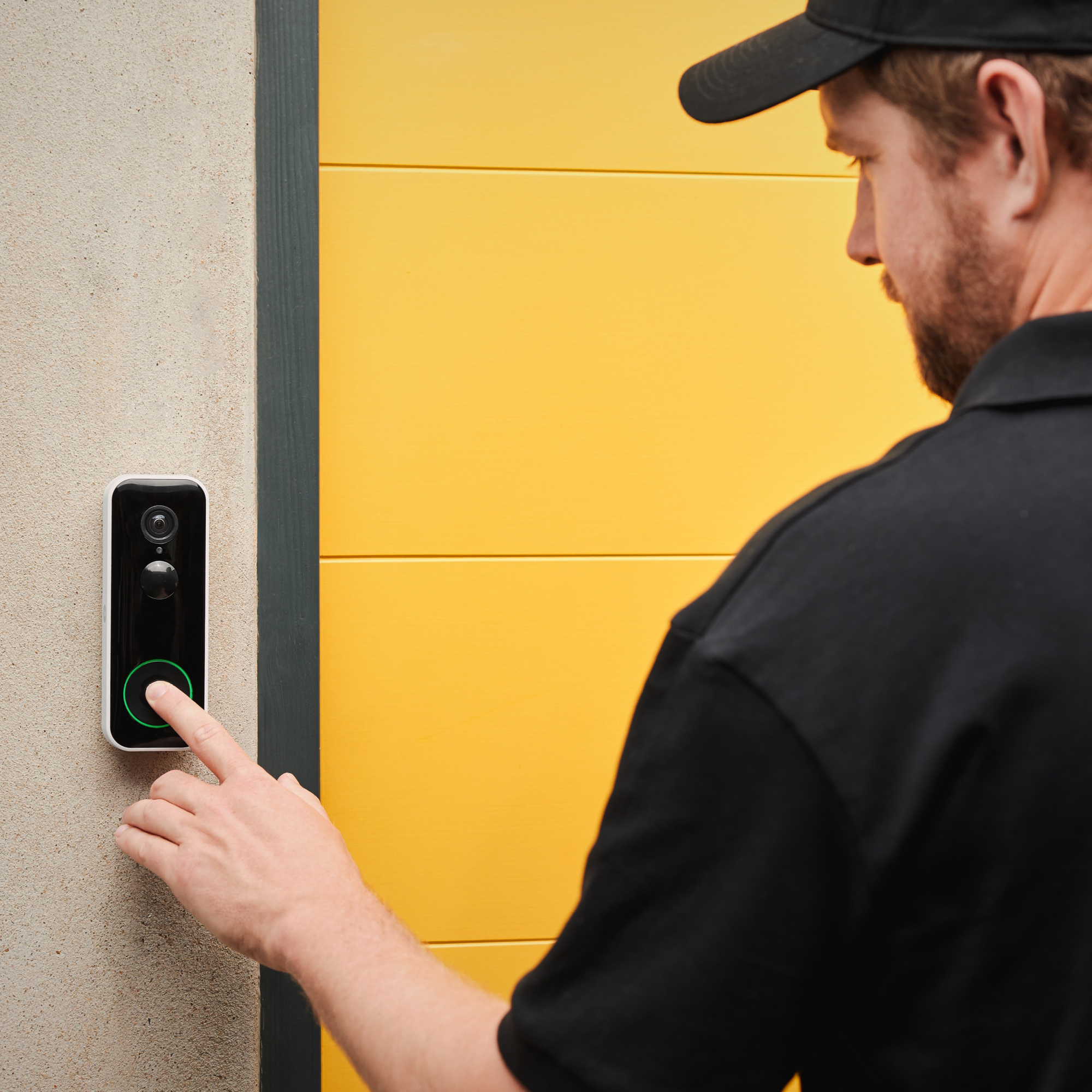 Un hombre de negro presiona un timbre en una pared junto a una puerta amarilla.