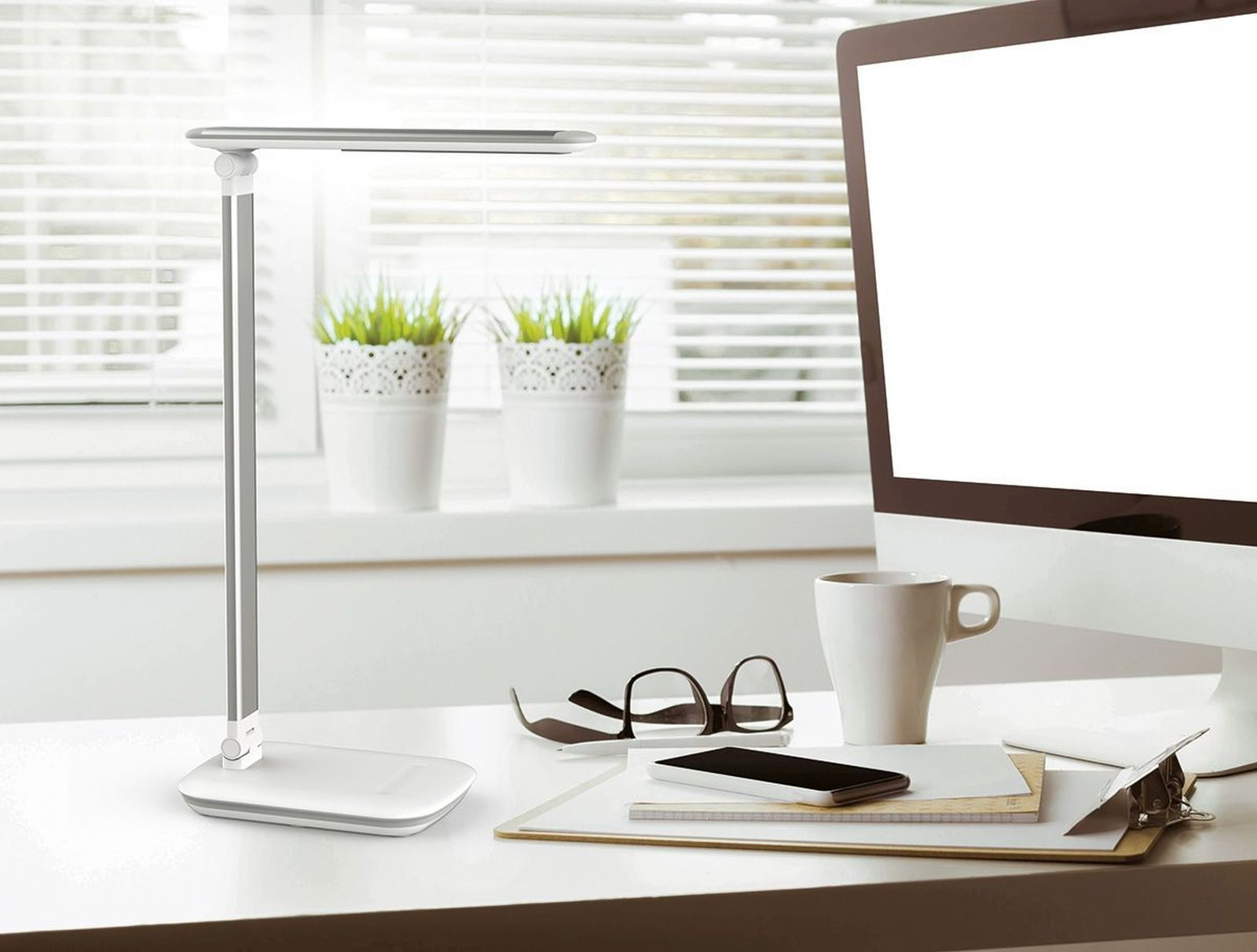 Una scrivania moderna con lampada, computer, tazza e occhiali.