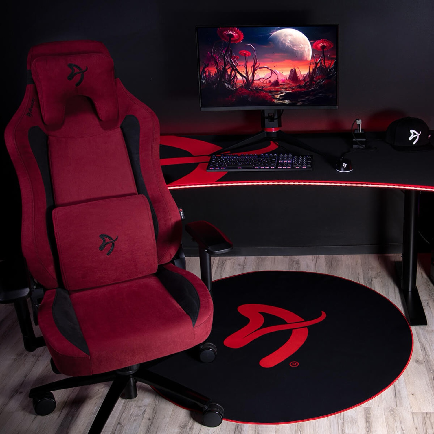Una sedia da gaming rossa accanto a una scrivania con monitor, tastiera e mouse.