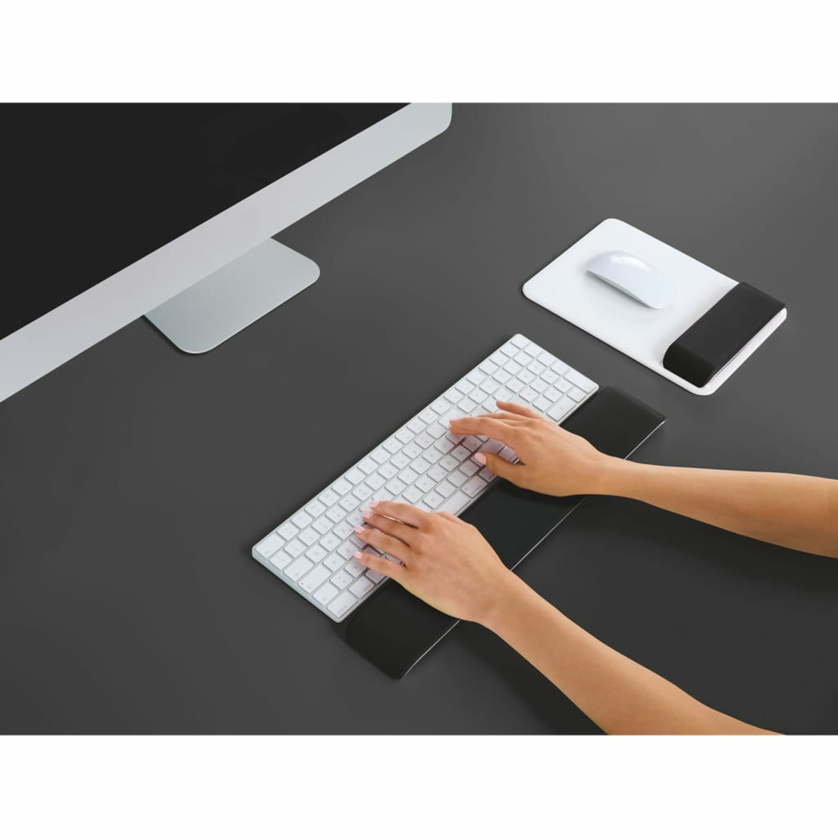 Mani che digitano su una tastiera bianca con poggiapolsi, accanto a un monitor e un mouse.