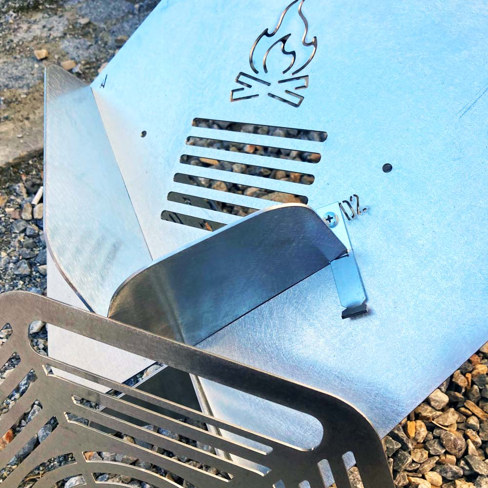 Alev logosu ve ızgara teli olan gümüş metal taşınabilir kamp ateşi ızgarası.