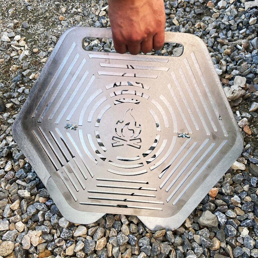 Bir el, taşların üzerinde alev desenli altıgen metal ızgara tutuyor.
