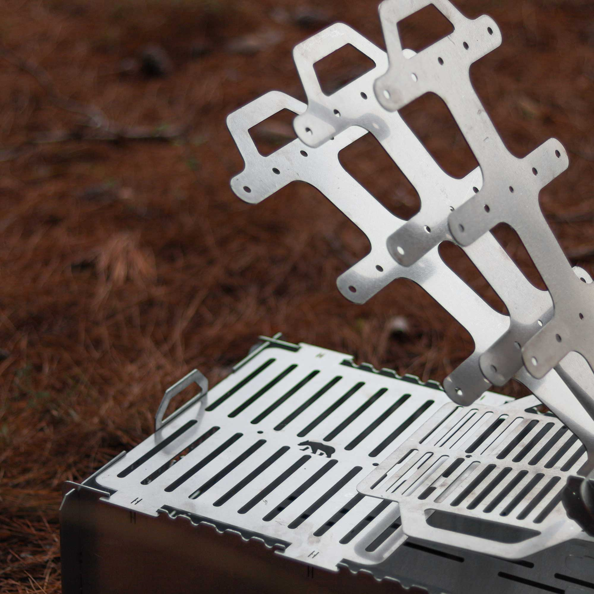 Sökülebilir metal mangal, çam iğneleriyle kaplı kahverengi zeminde duruyor.