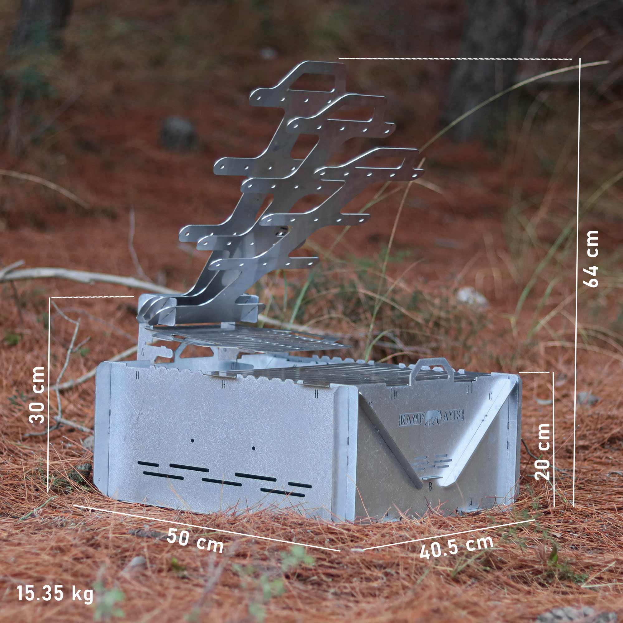 Gümüş rengi metal bir mangal, çam iğneleriyle kaplı orman zemininde duruyor.