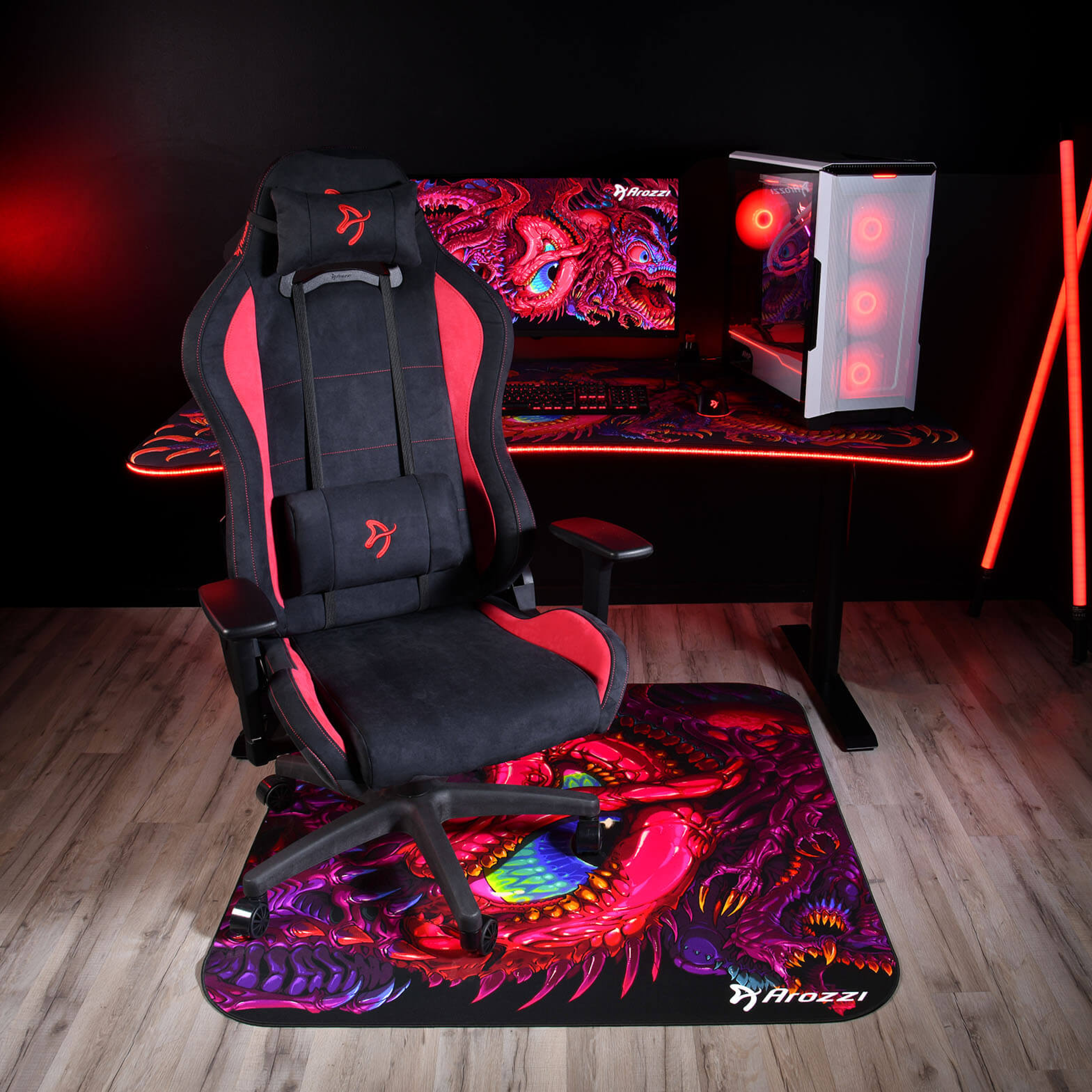 Een zwarte en rode gamestoel staat voor een bureau met pc en monitor.