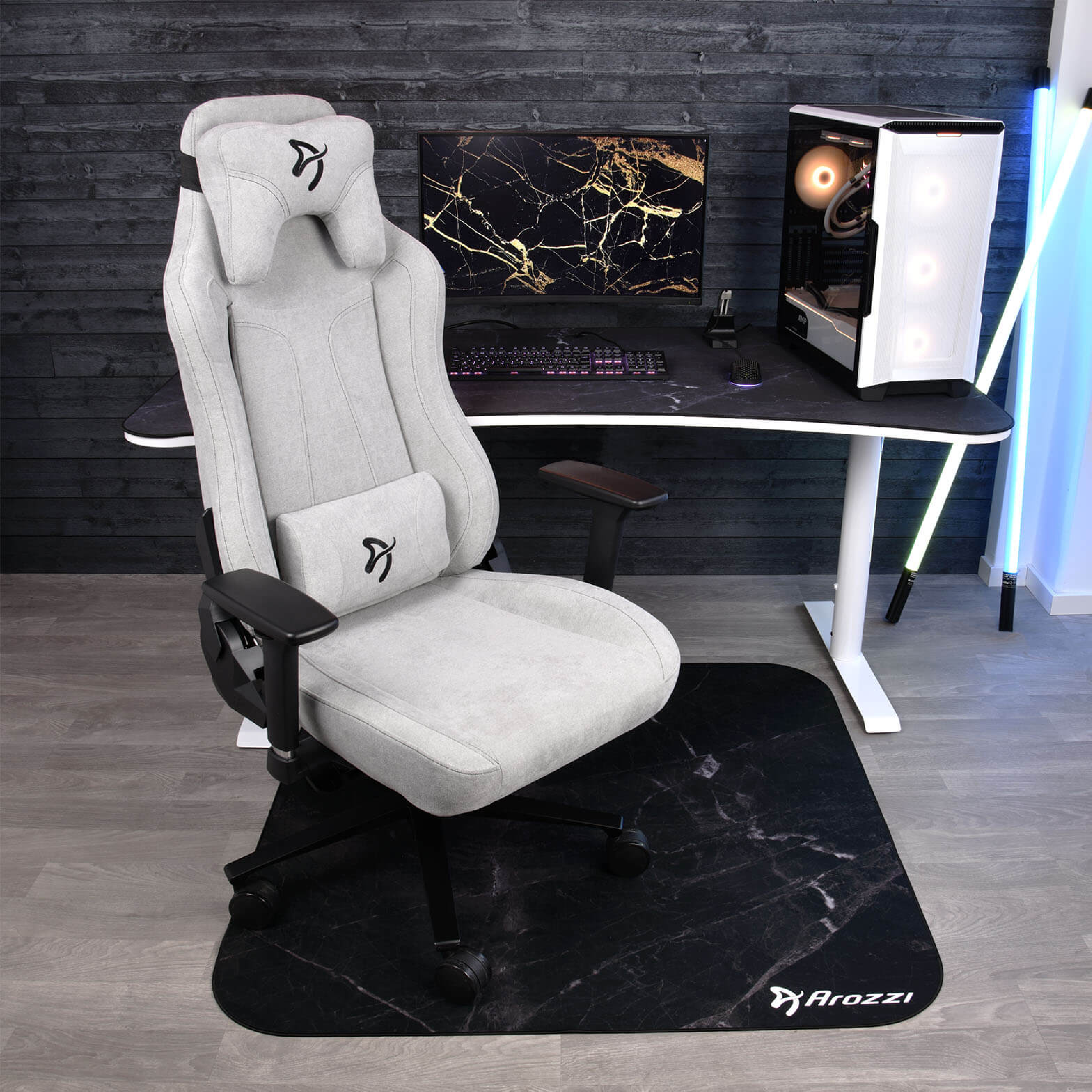 Ein heller Gaming-Stuhl mit Kopf- und Lendenkissen vor einem Schreibtisch mit PC.