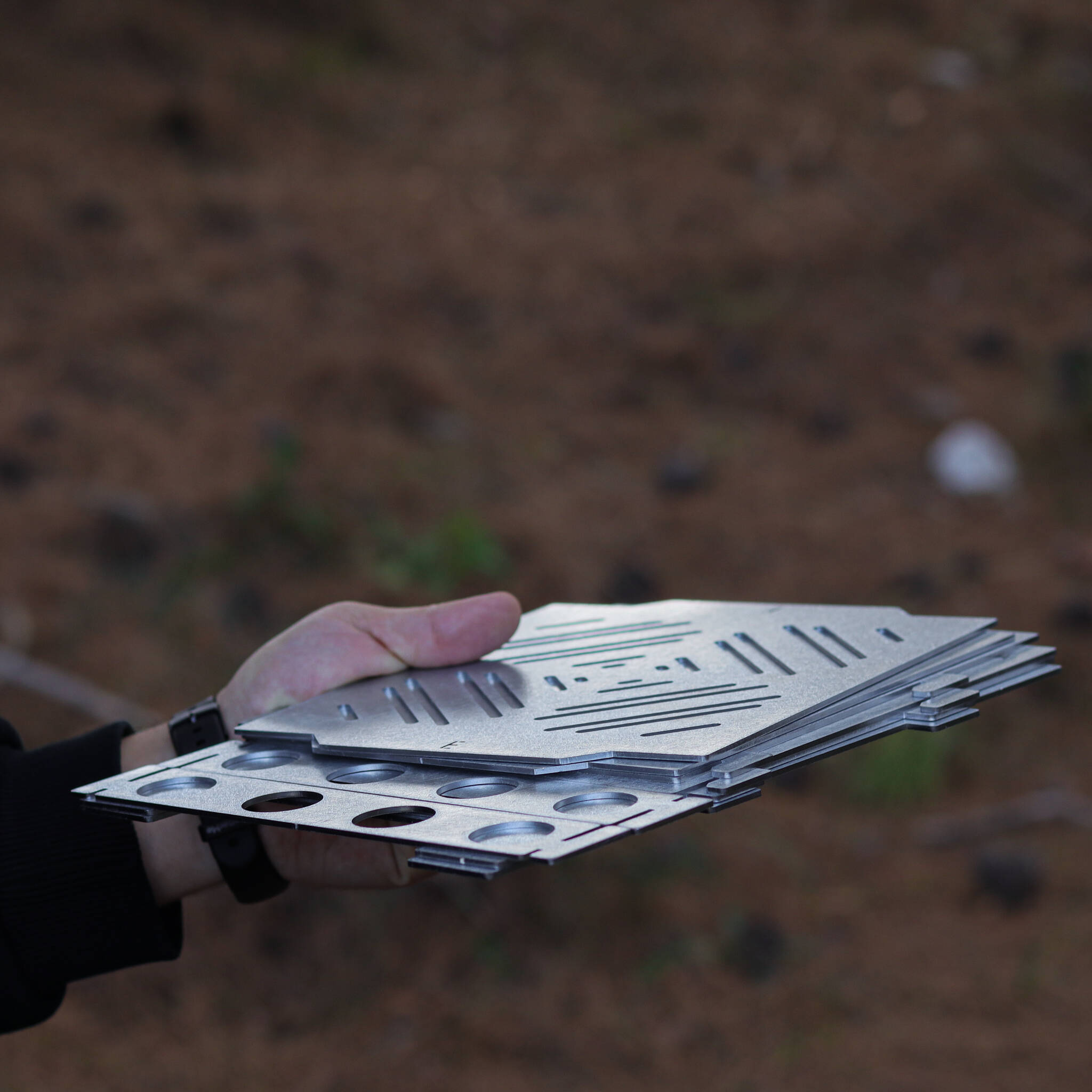 Bir el, yuvalar ve daireler içeren yığılmış metal plakalar tutuyor.