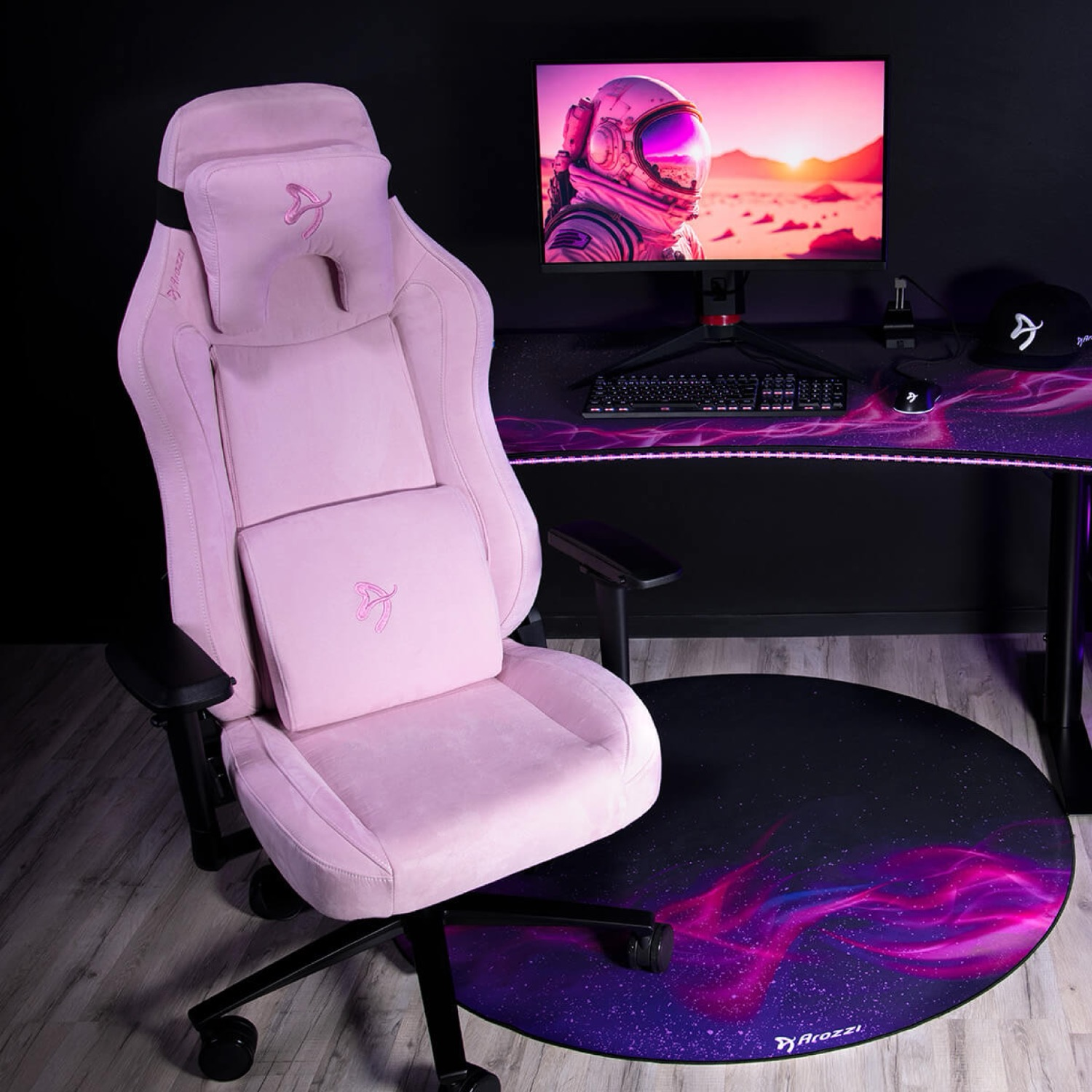 Ein rosa Gaming-Stuhl steht neben einem Schreibtisch mit einem Monitor, der einen Astronauten zeigt.