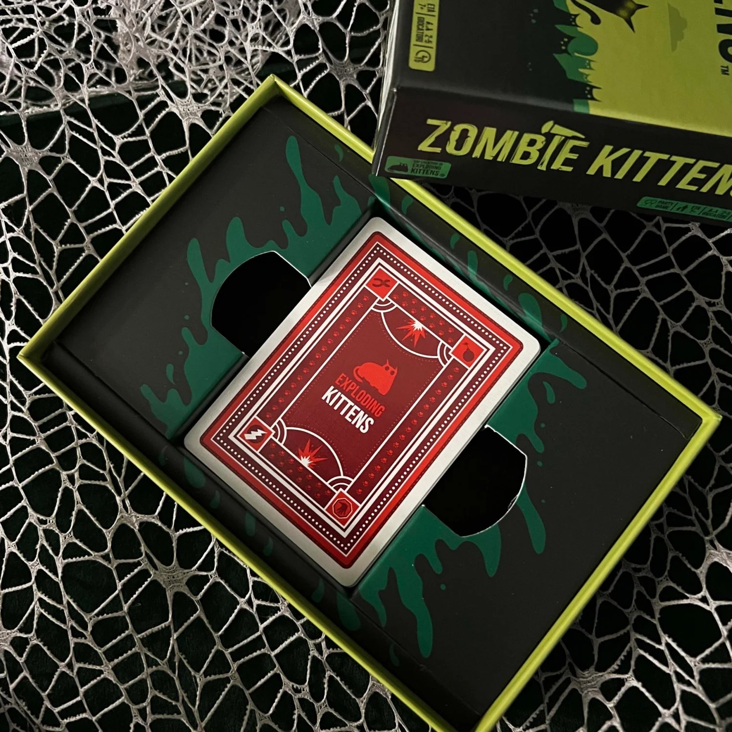 Eine offene Spielschachtel mit einer Karte von Exploding Kittens und der Zombie Kittens-Box.