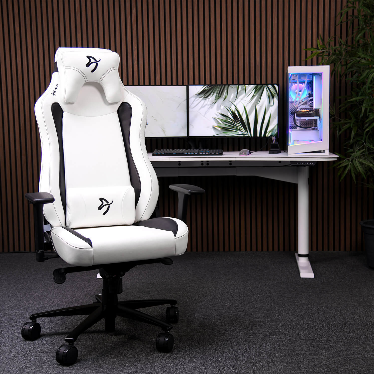 Een witte gamestoel staat voor een bureau met twee monitoren en een pc.