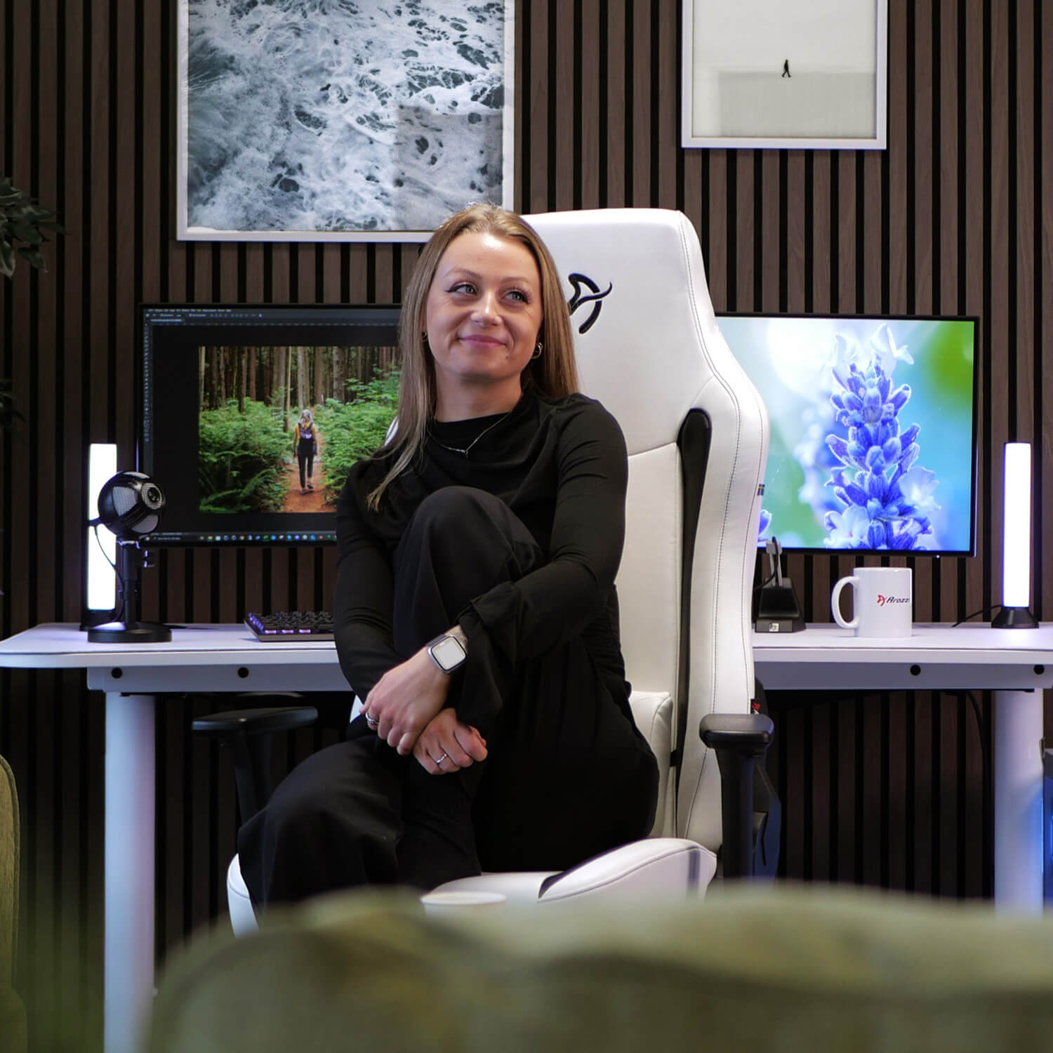 Een vrouw zit in een witte gamestoel voor een bureau met monitoren.