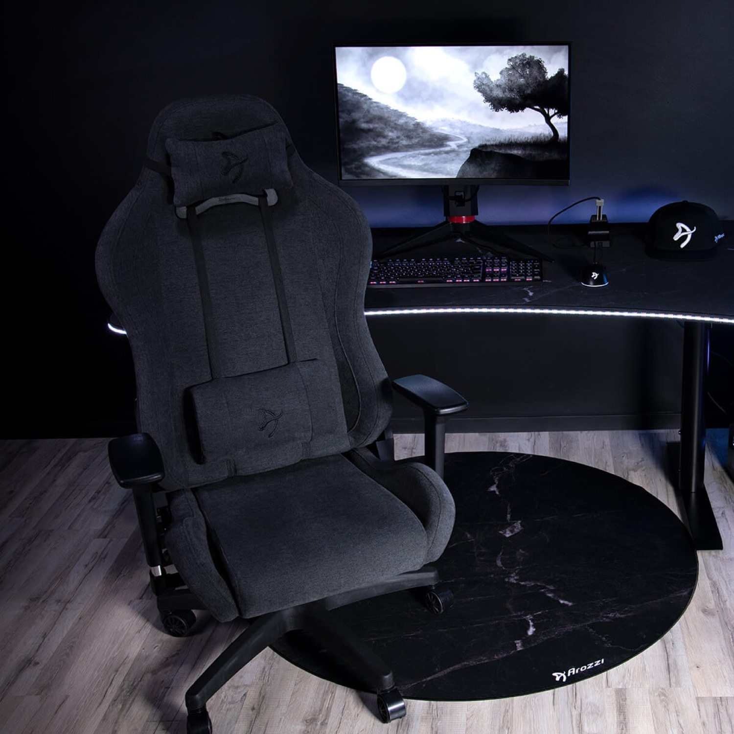 Ein dunkler Gaming-Stuhl steht auf einem Marmormuster-Teppich vor einem Schreibtisch mit Monitor.
