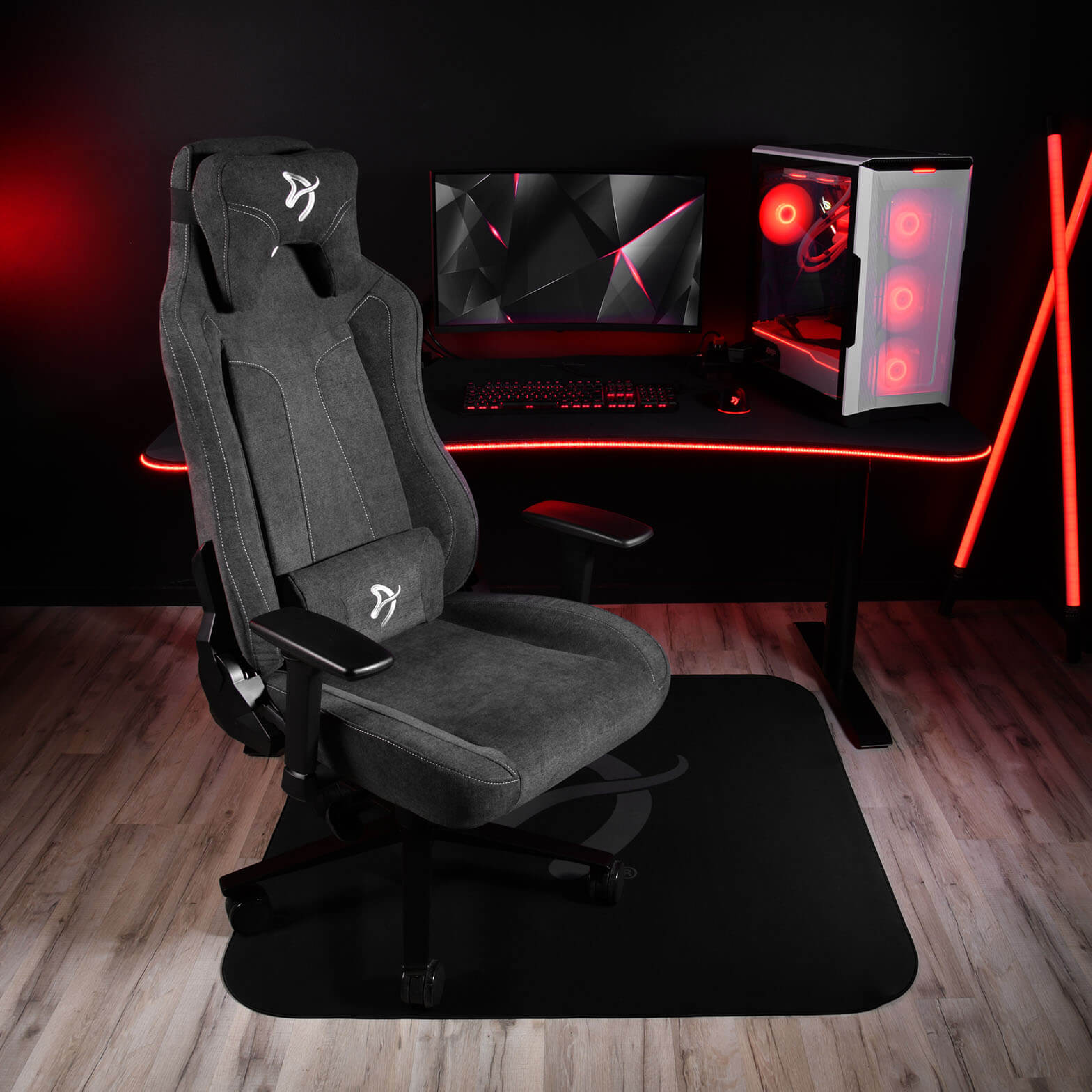 Een donkere gamestoel voor een bureau met pc, monitor en toetsenbord.