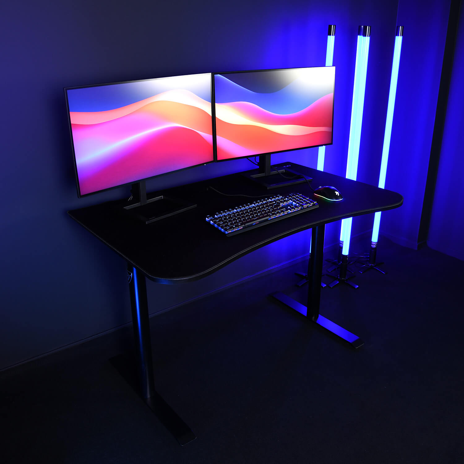 Una scrivania nera con due monitor, tastiera e mouse, illuminata da luci a tubo blu.