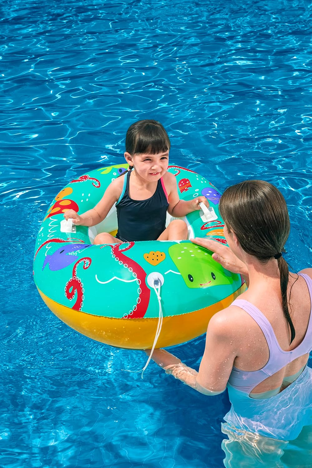 Ein Kind sitzt in einer bunten aufblasbaren Pool-Schwimmhilfe, während eine Frau sie in blauem Wasser festhält.