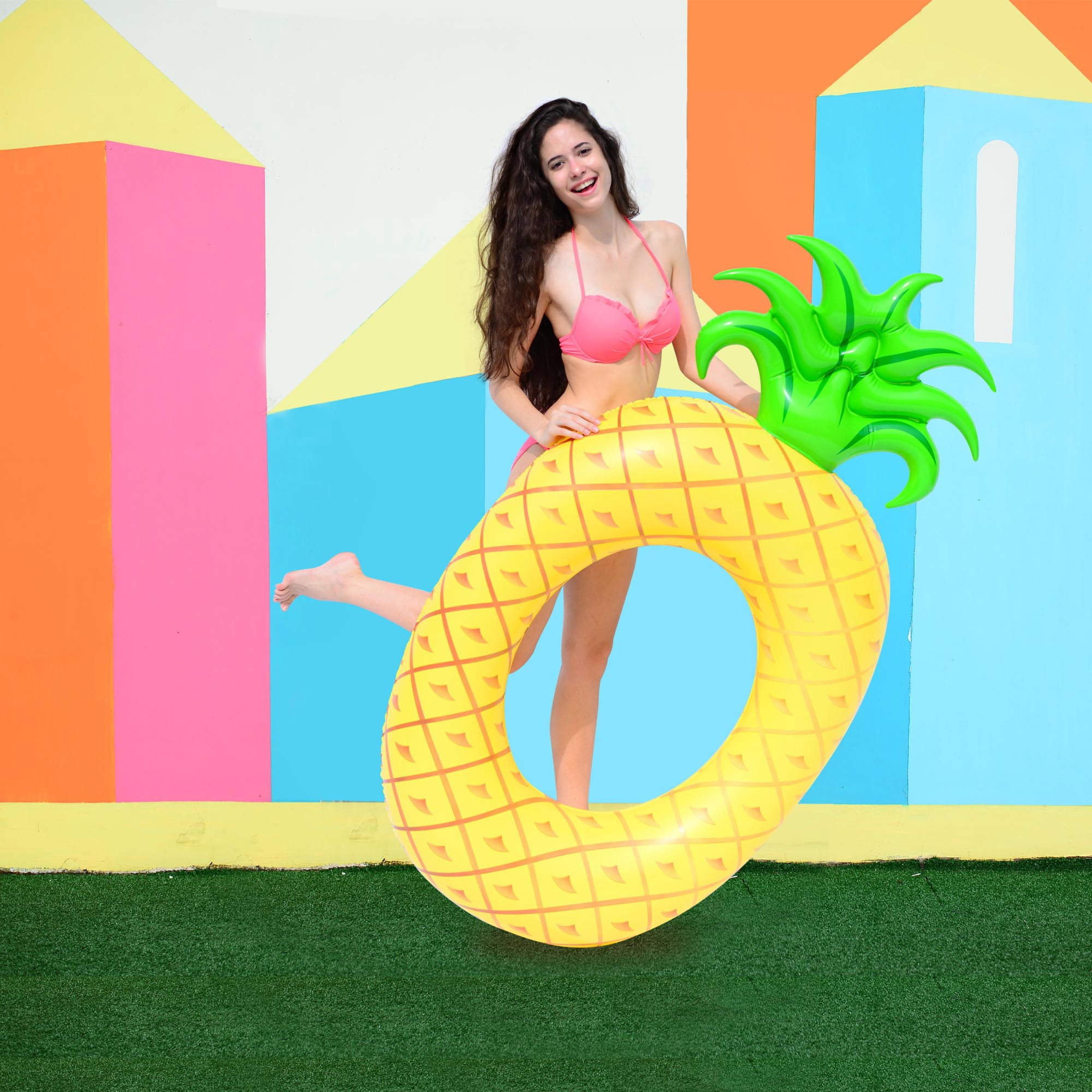 Frau im Bikini mit aufblasbarer Ananas, bunte geometrische Kulisse.