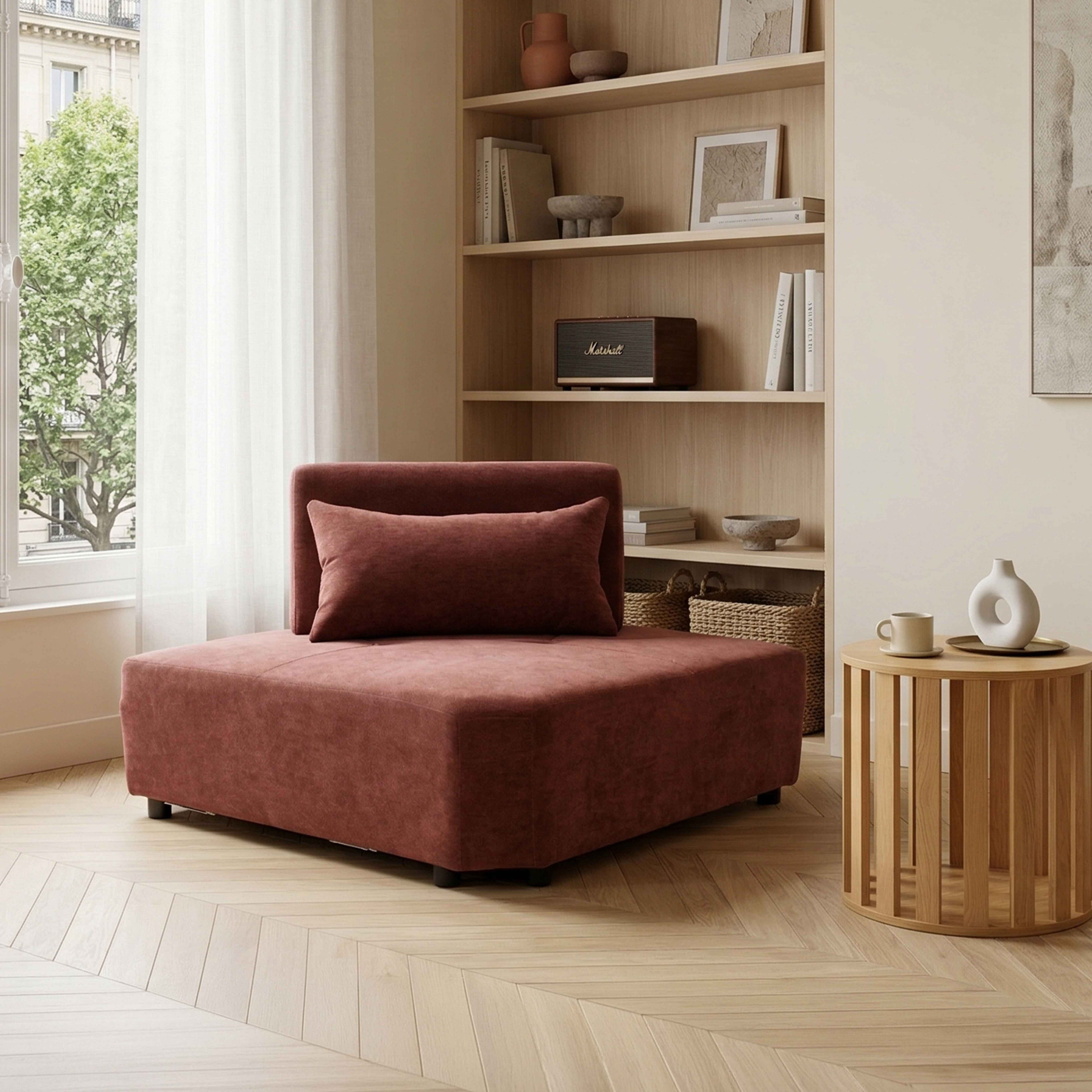 Ein korallfarbener Sessel mit Kissen steht auf einem Holzboden vor einem Regal.
