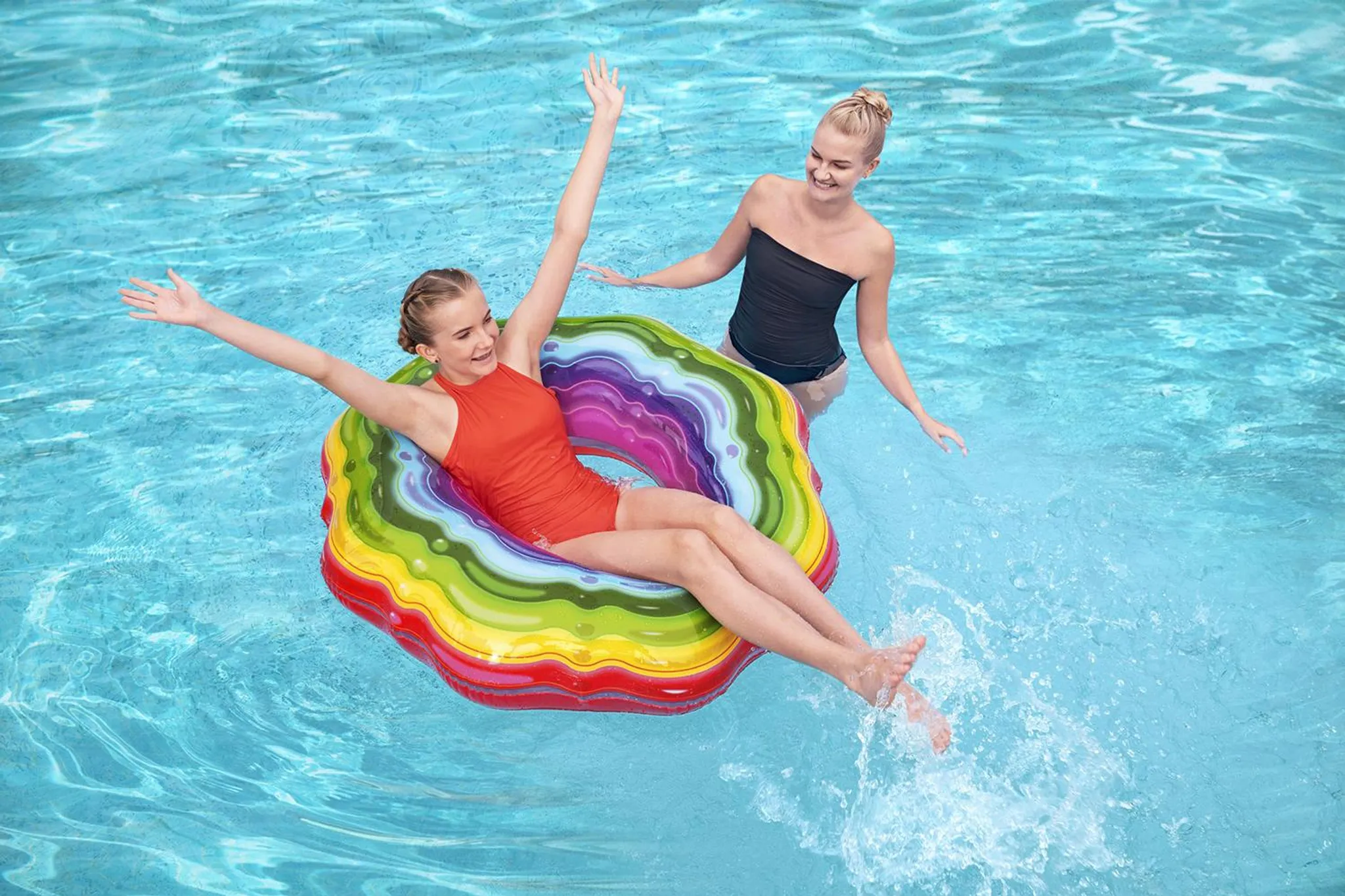 Zwei Mädchen planschen im Pool, eines auf einem bunten Schwimmring, das andere steht.