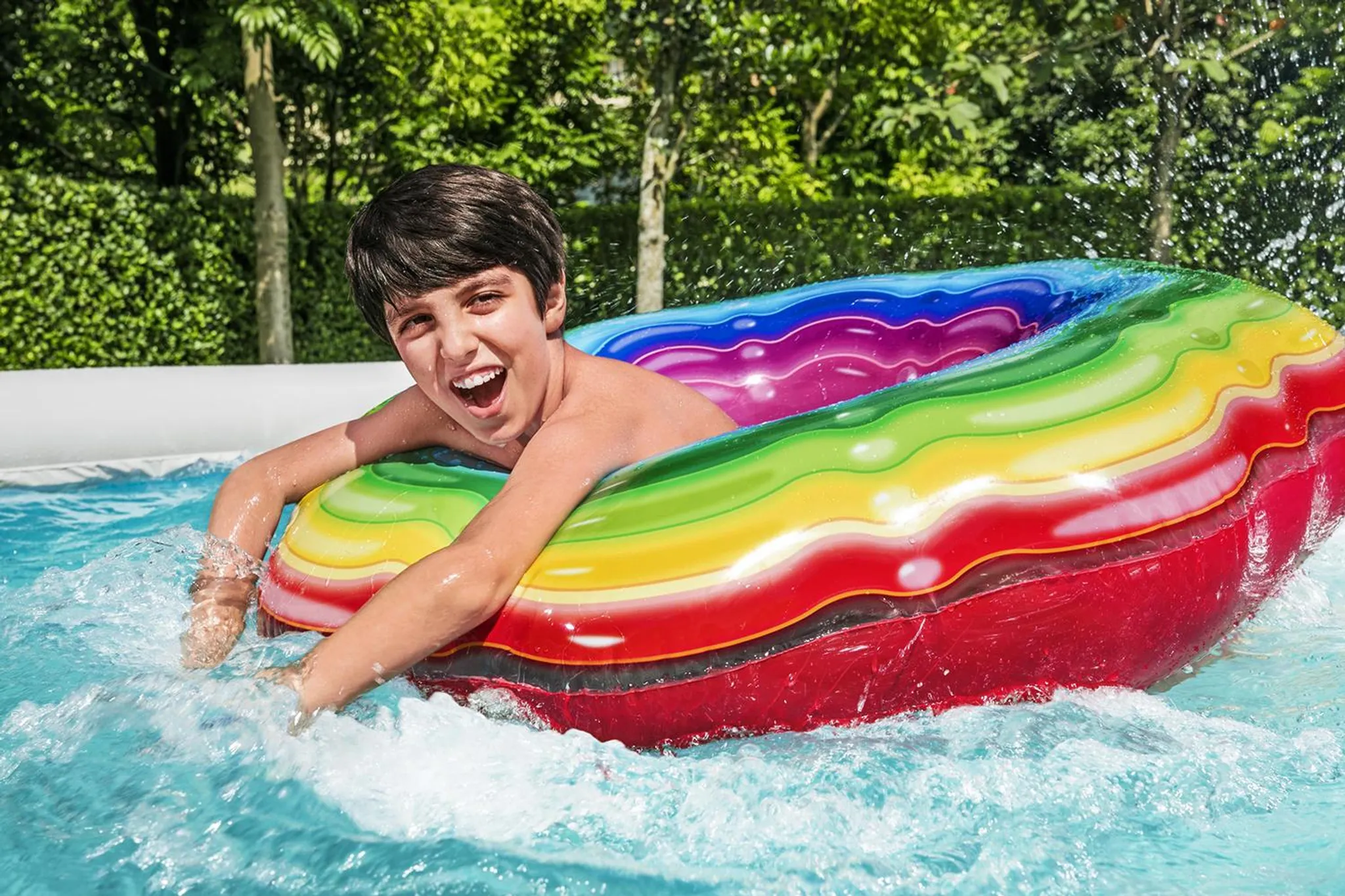 Ein Junge planscht in einem Pool auf einem bunten aufblasbaren Schwimmring.