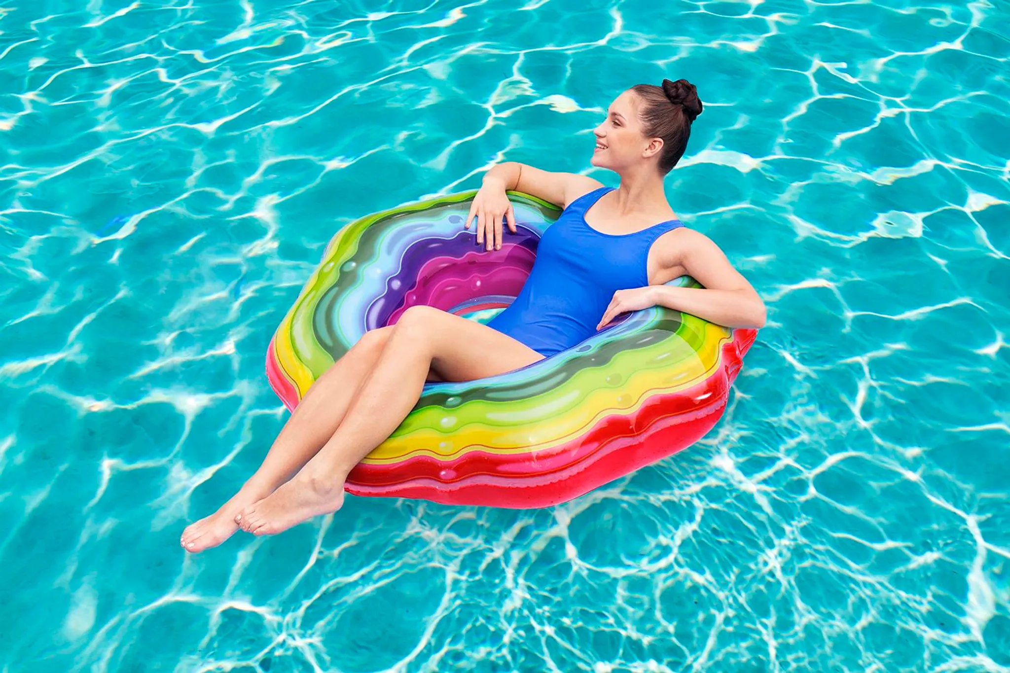 Eine Frau in einem blauen Badeanzug schwimmt auf einem bunten Schwimmring im Pool.