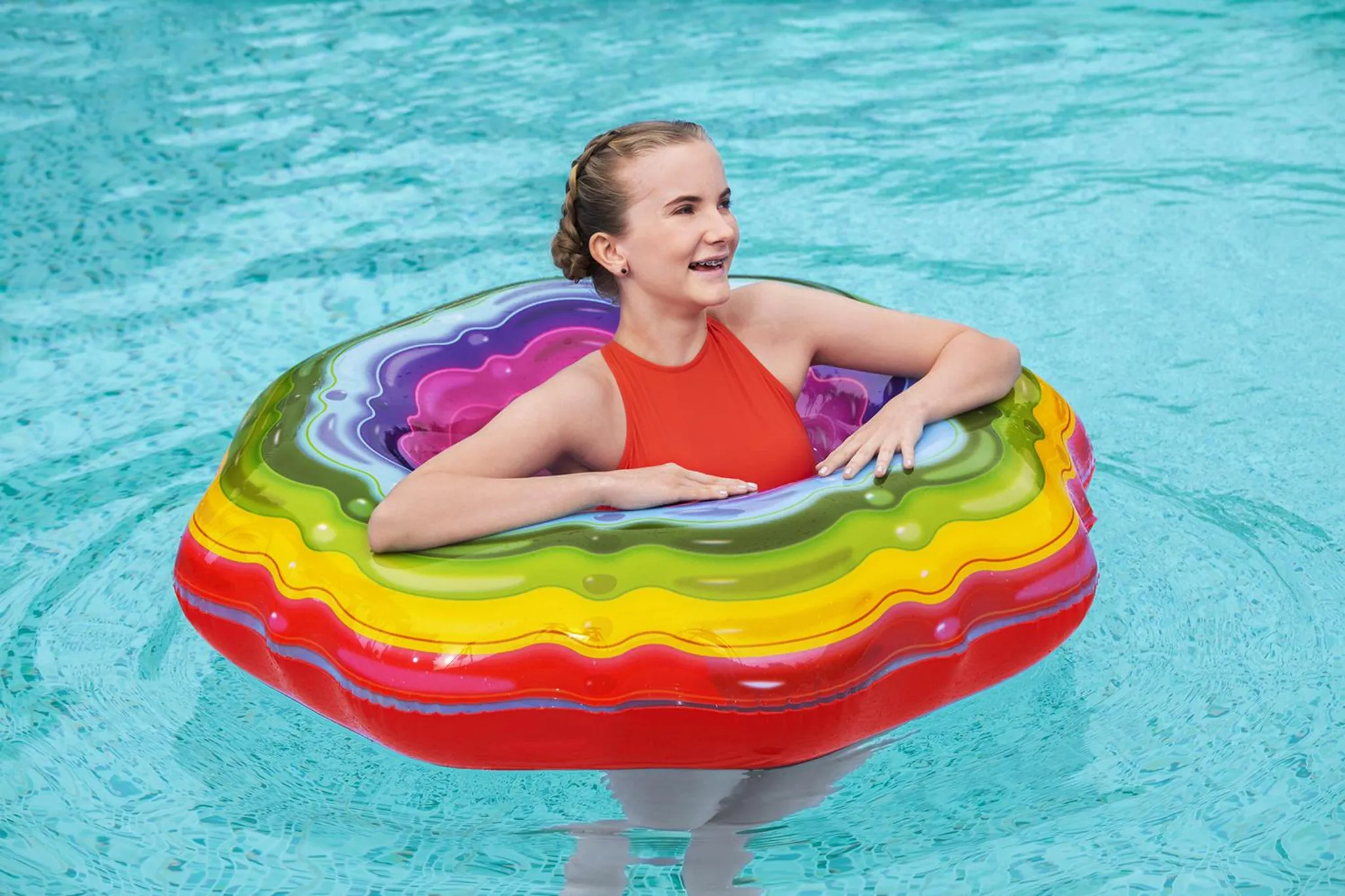 Ein Mädchen mit einem orangefarbenen Badeanzug sitzt in einem bunten Schwimmring im Pool.