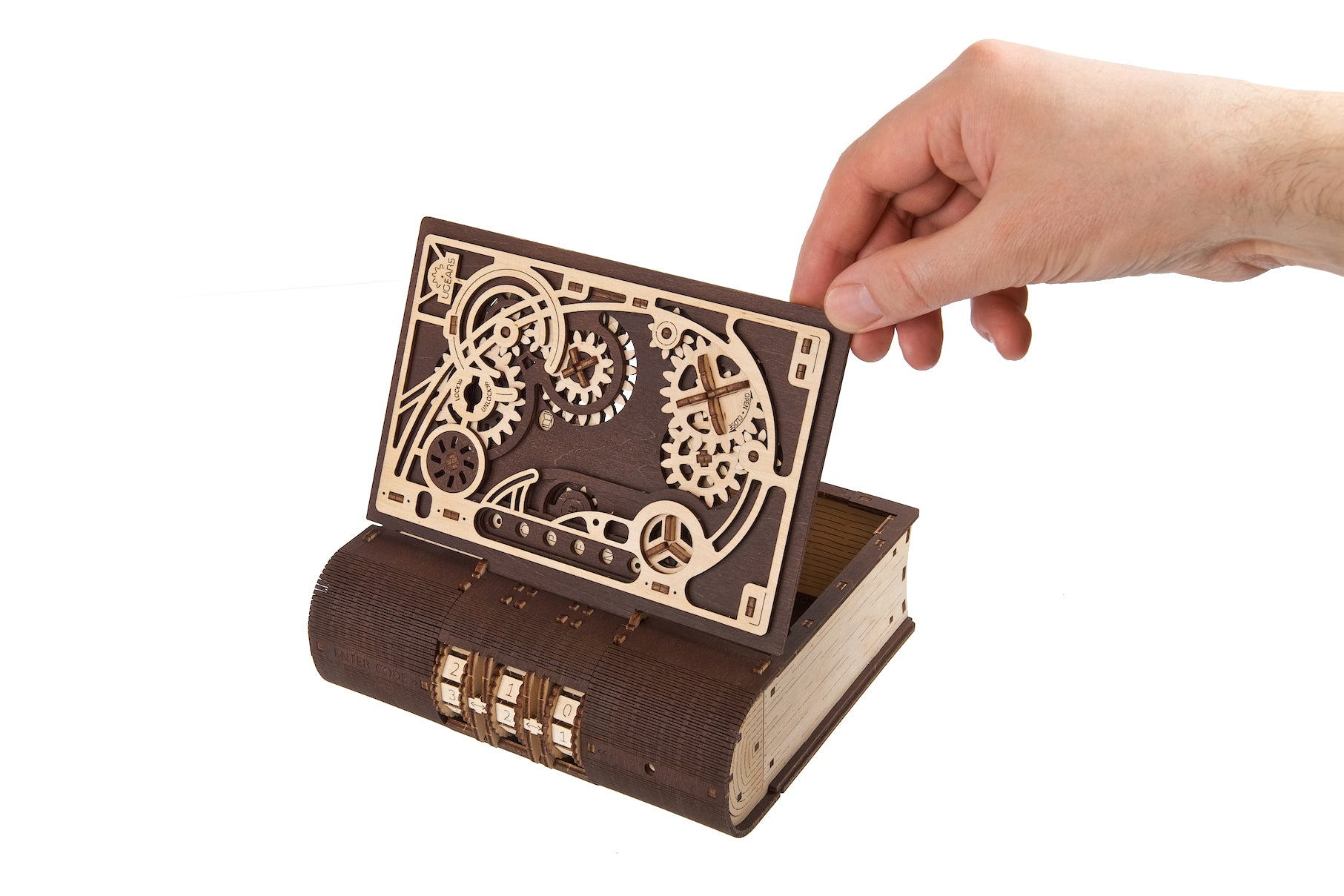 Eine Hand hebt den hölzernen Kassettenbanddeckel von einer buchförmigen Kiste mit Zahnrädern.