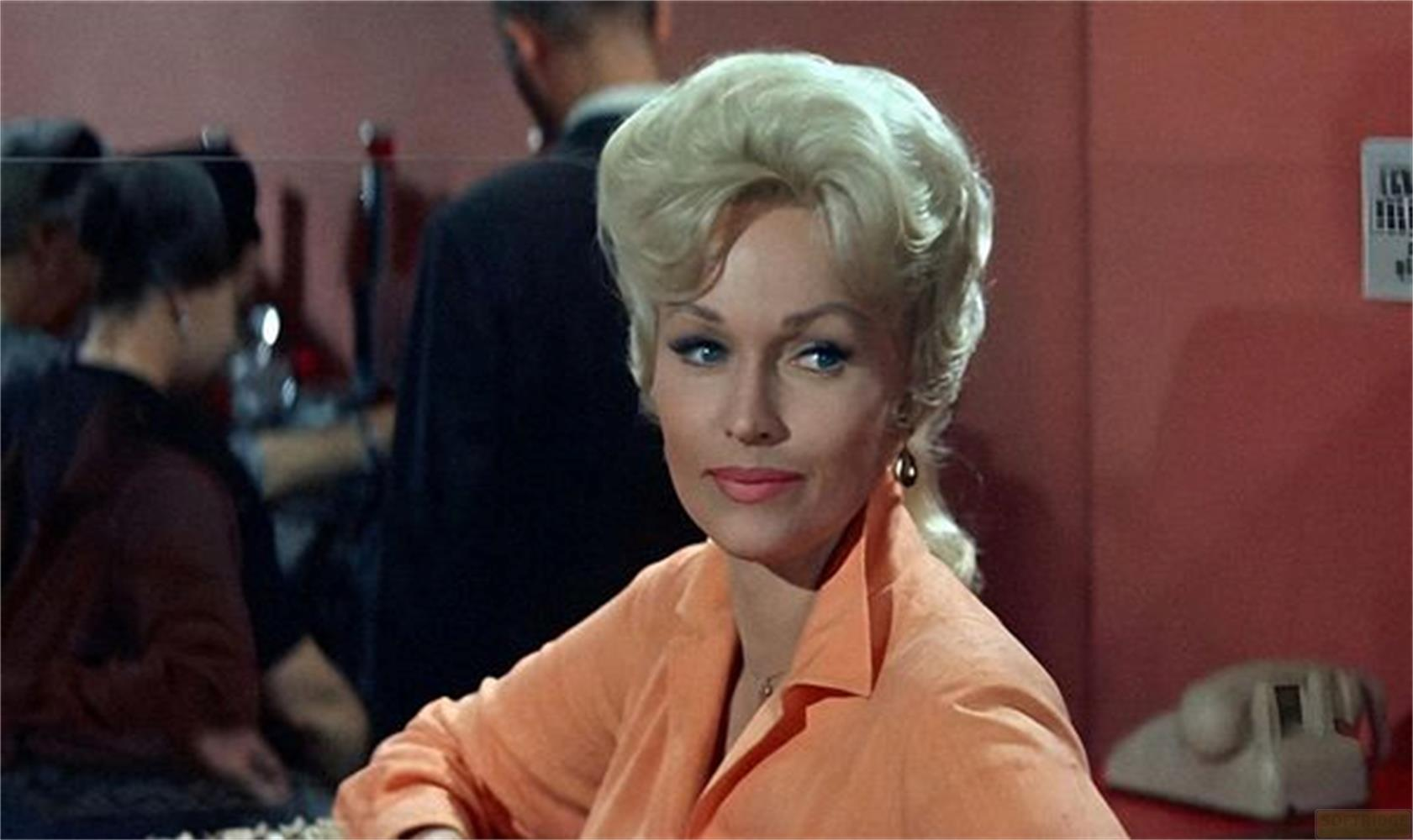 Eine Frau mit blonden Haaren und einem orangefarbenen Hemd blickt nach rechts.