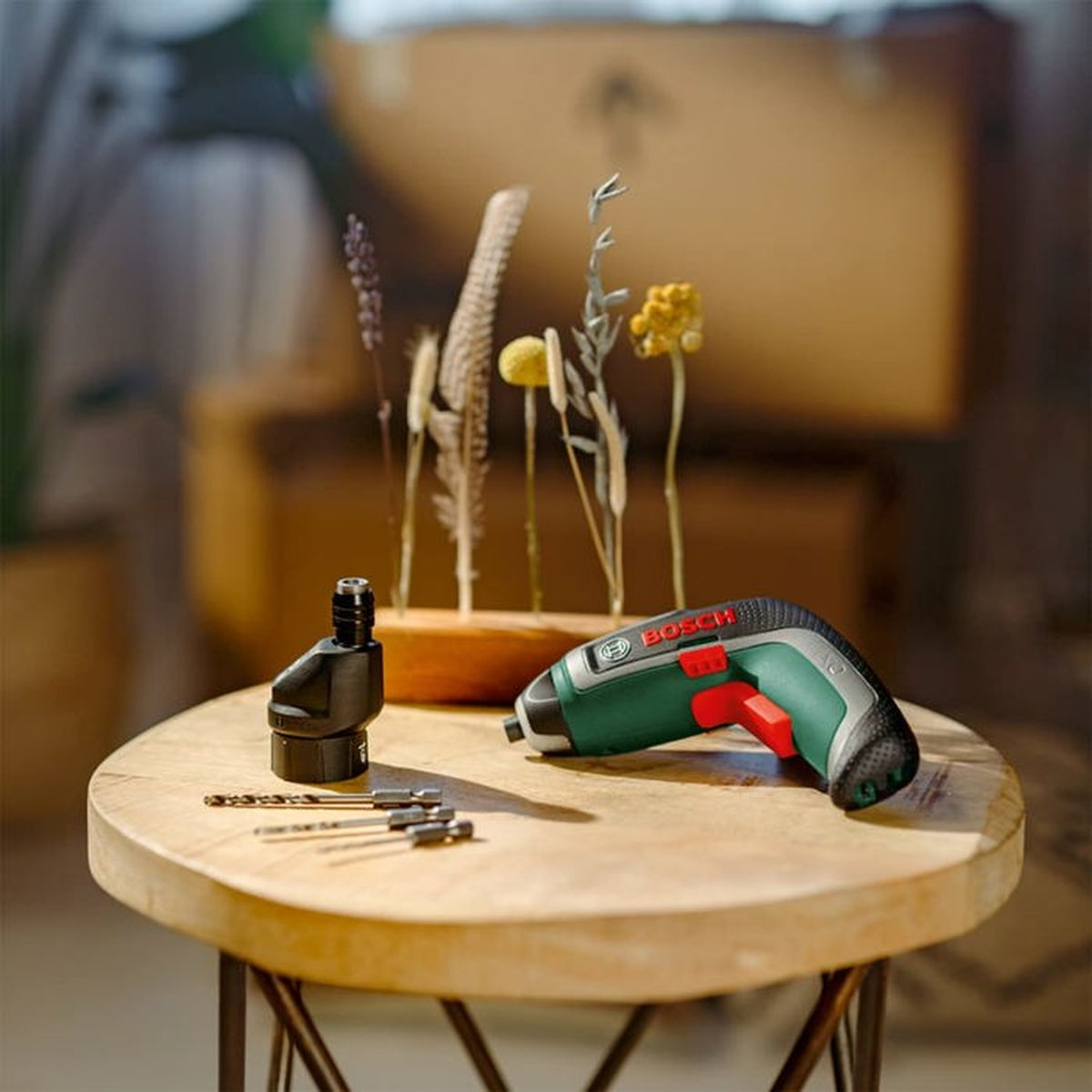 Grüner Bosch Schrauber mit Bits und Trockenblumen auf rundem Holztisch.