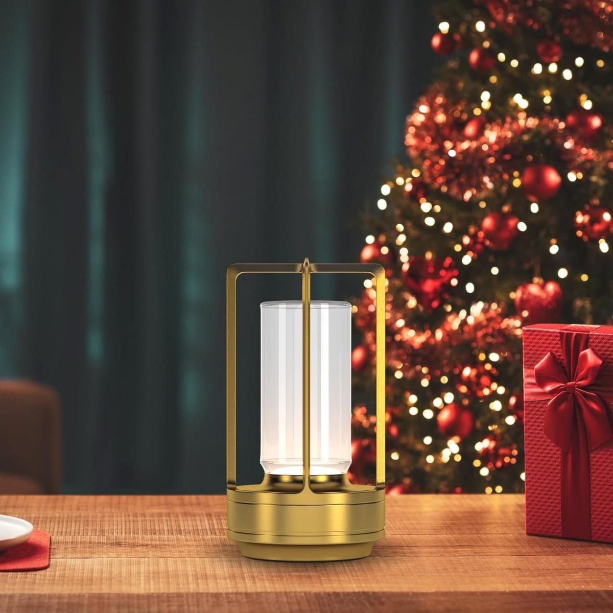 Eine goldene Lampe steht auf einem Holztisch vor einem Weihnachtsbaum.