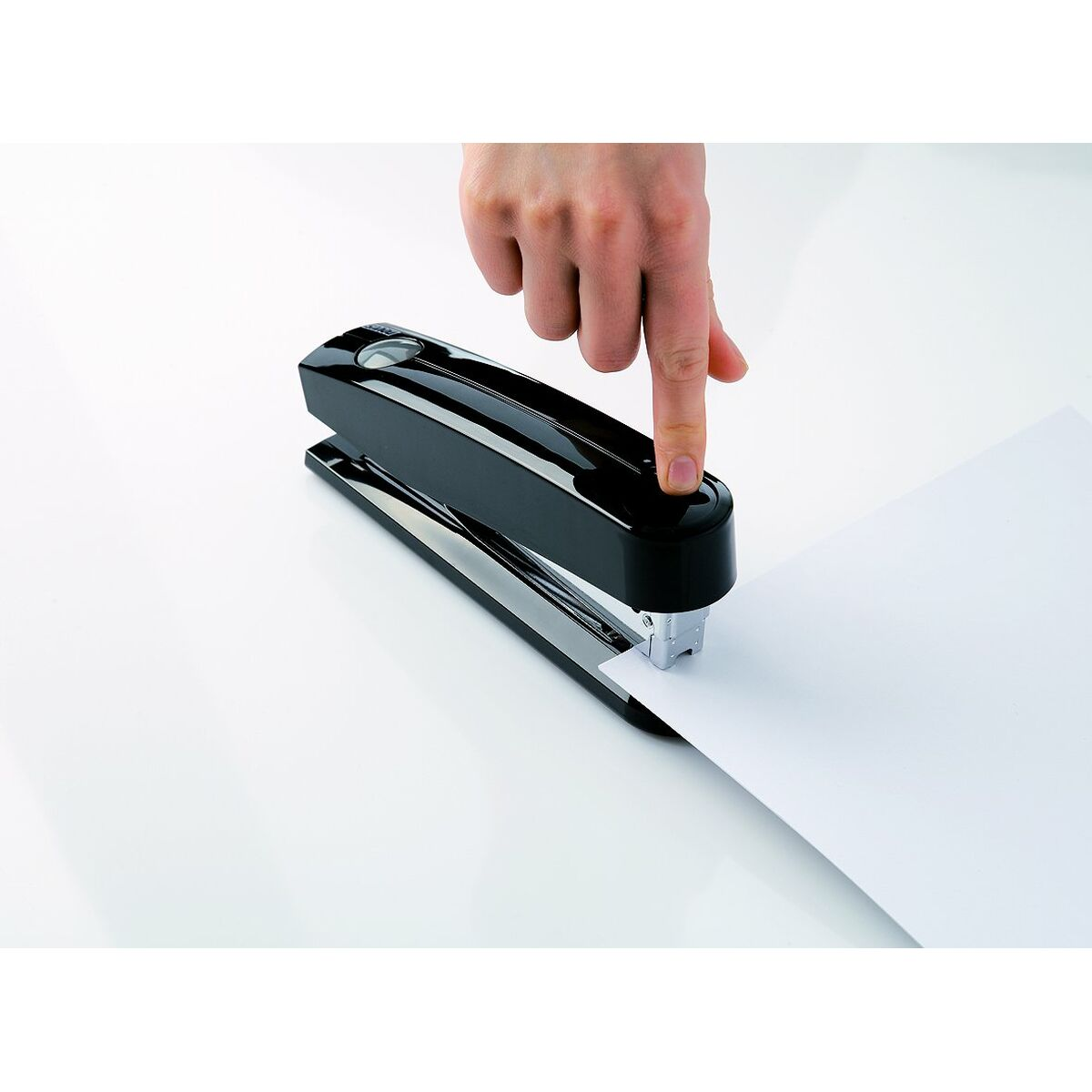 Eine Hand drückt einen schwarzen Hefter auf ein Blatt Papier.
