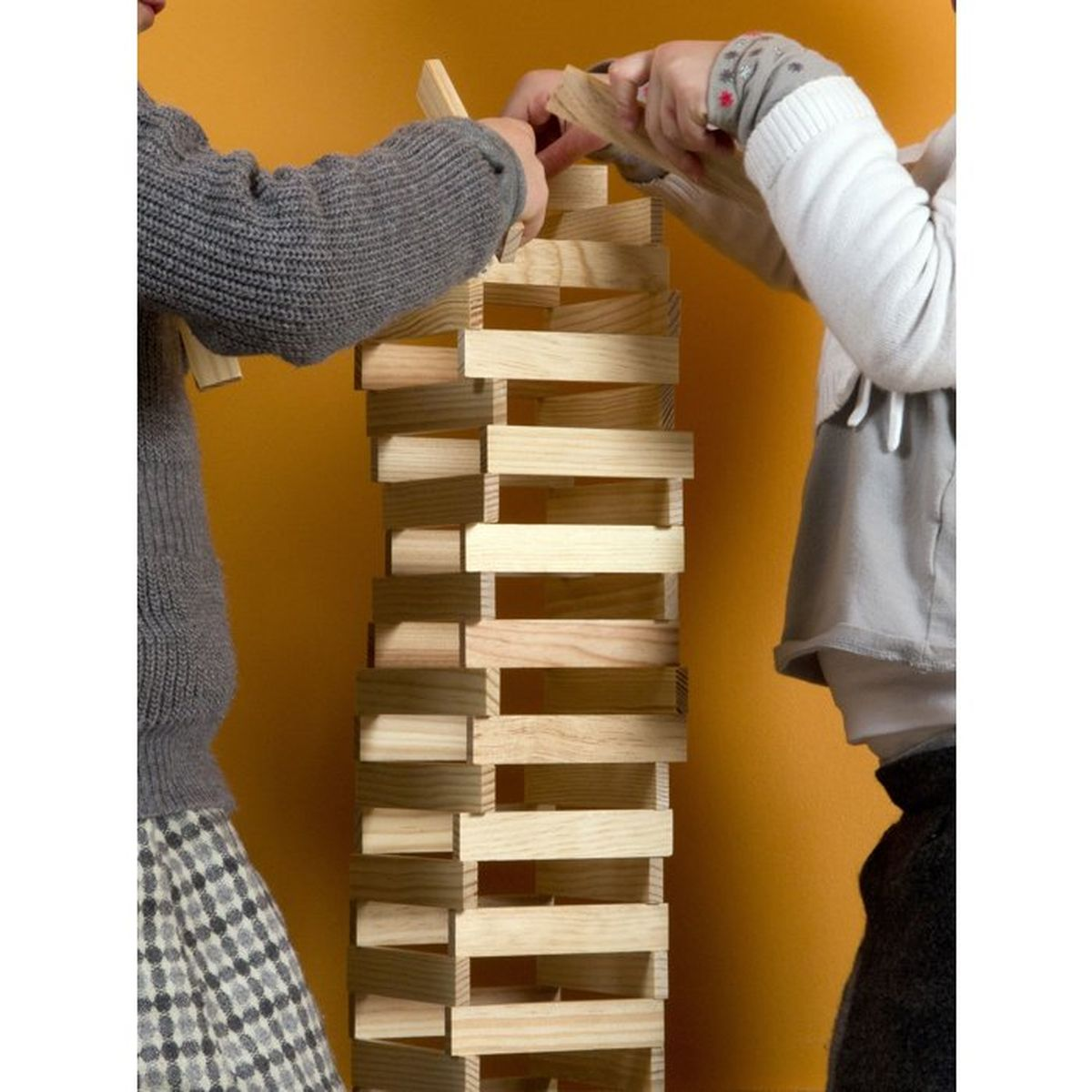 Bambini costruiscono un'alta torre di blocchi di legno su sfondo arancione.