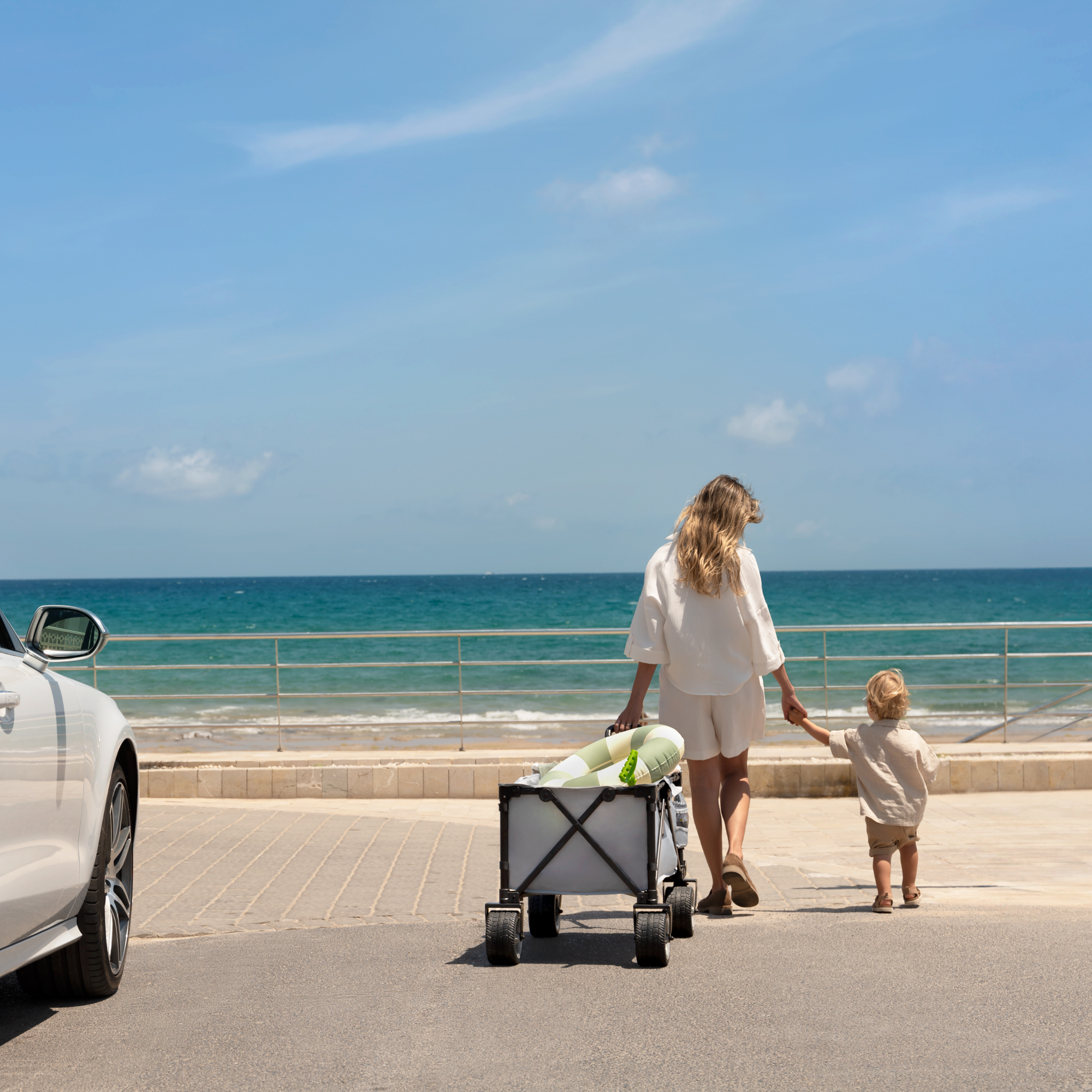 Eine Frau und ein Kind gehen am Meer entlang, schieben einen Wagen.