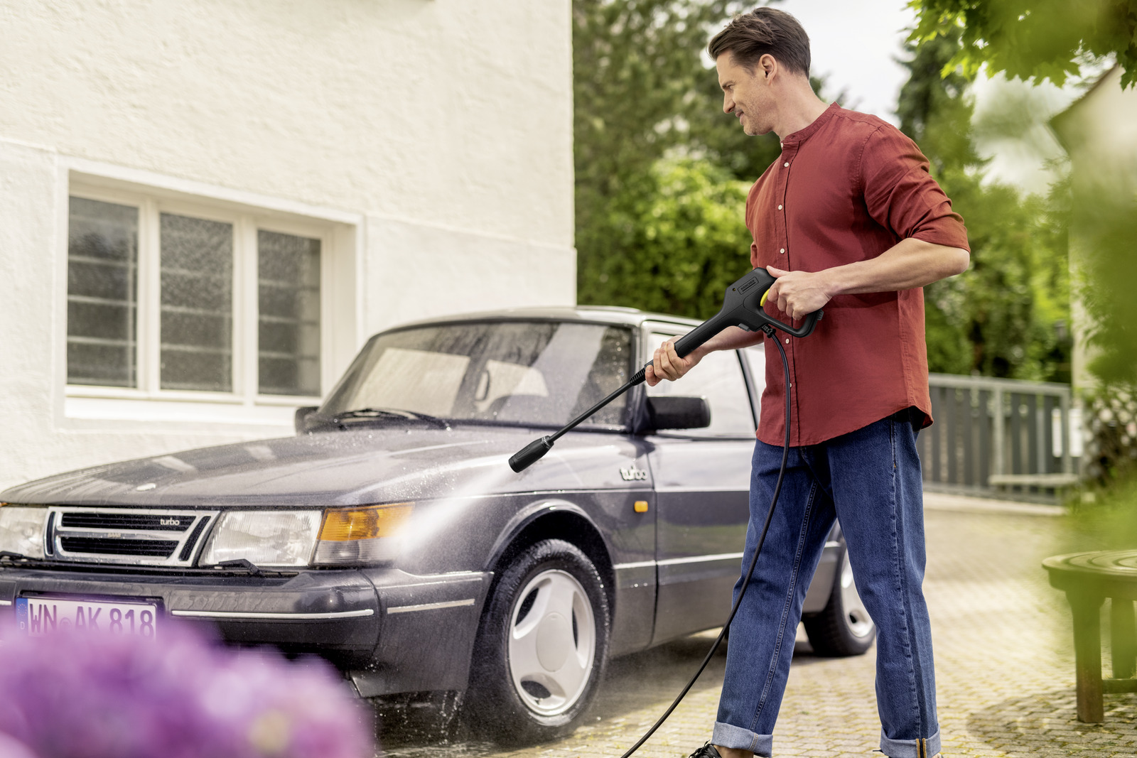 Mann wäscht ein Auto mit einem Hochdruckreiniger im Freien.