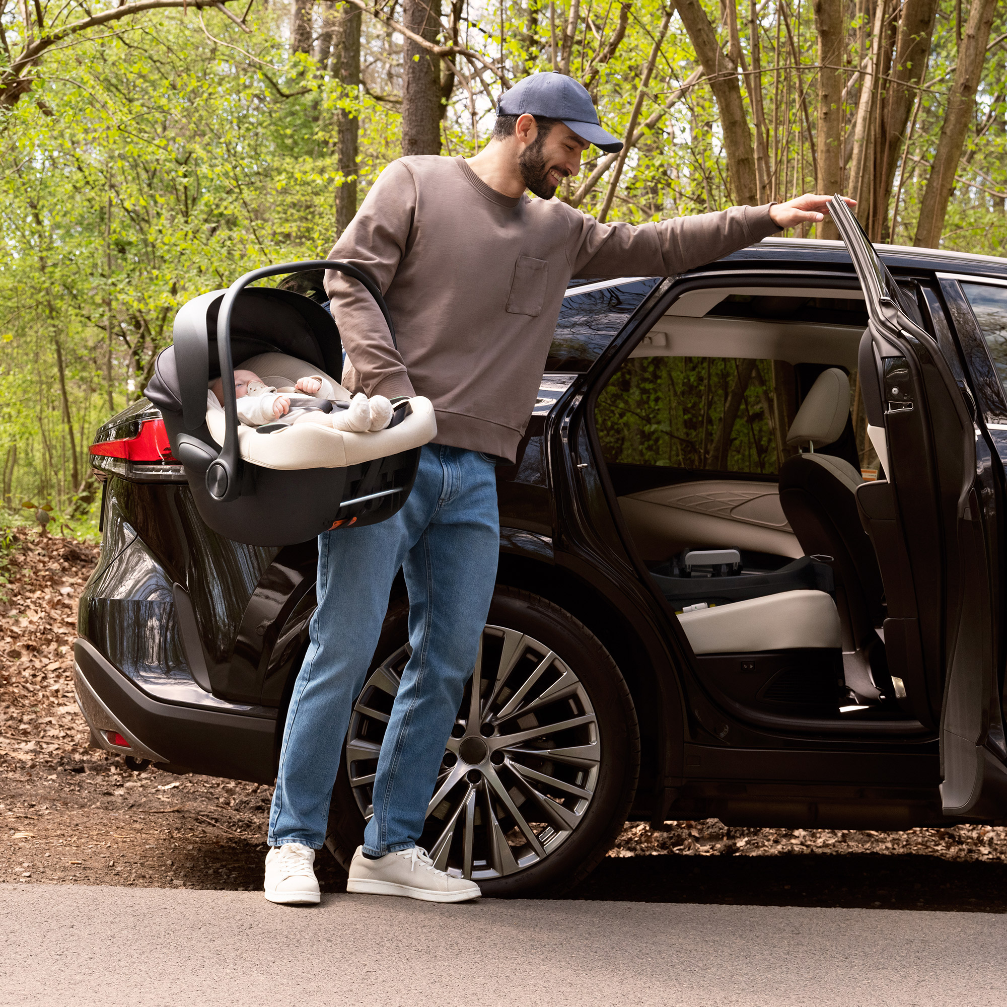 Mann mit Baby-Autositz steigt in dunkles Auto im Wald.