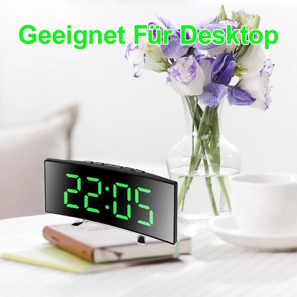 Ein digitaler Wecker zeigt 22:05 auf einem Tisch mit Blumen und einer Tasse.