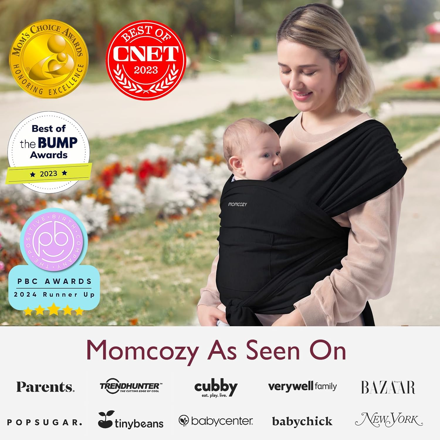Una donna porta un bambino in una fascia nera. Premi a sinistra. Momcozy.